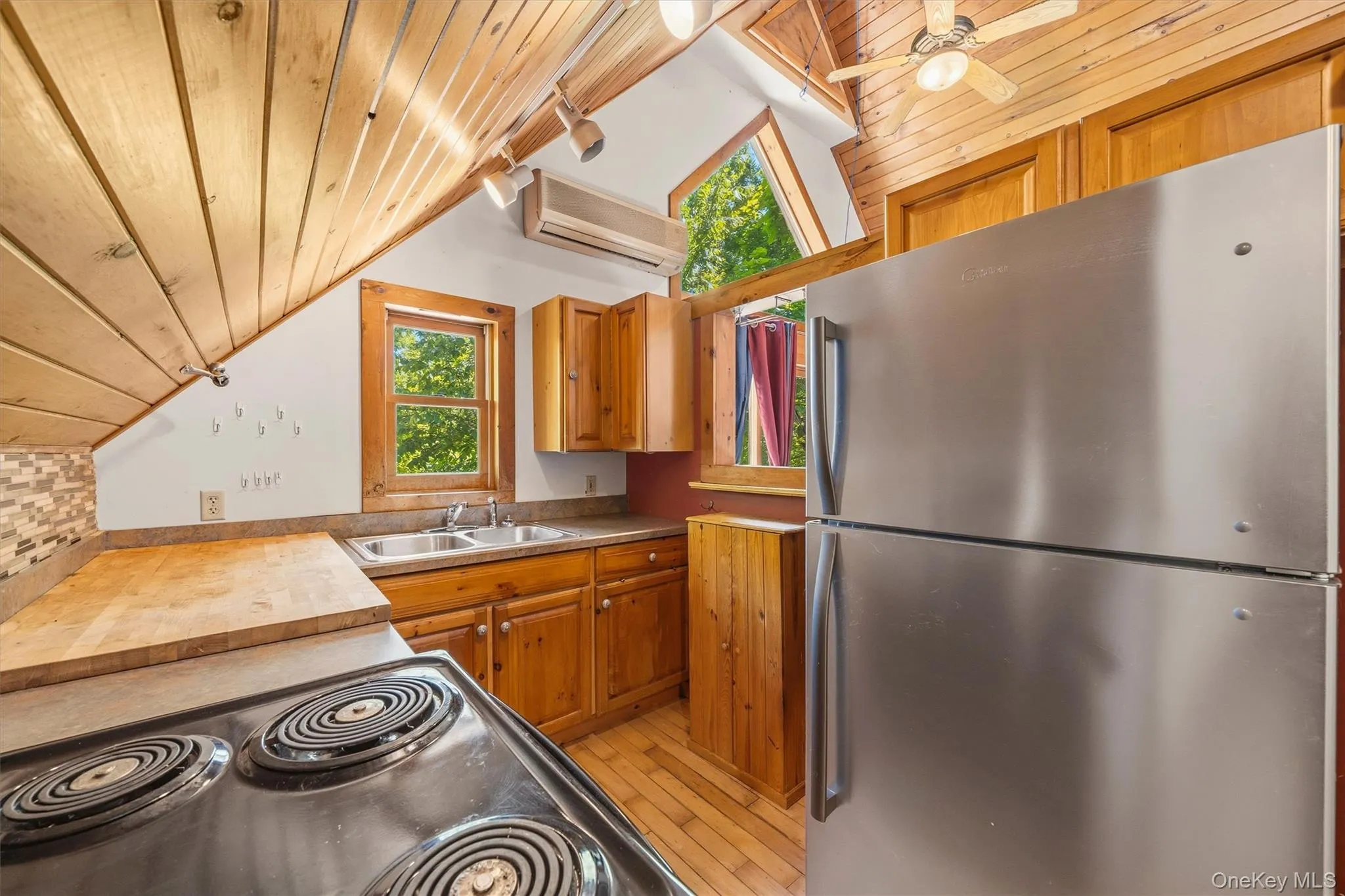 Kitchen featuring wood-finish flooring, wood cabinetry, a stainless steel refrigerator, and a double basin sink Kitchen featuring wood-finish flooring, wood cabinetry, a stainless steel refrigerator, and a double basin sink