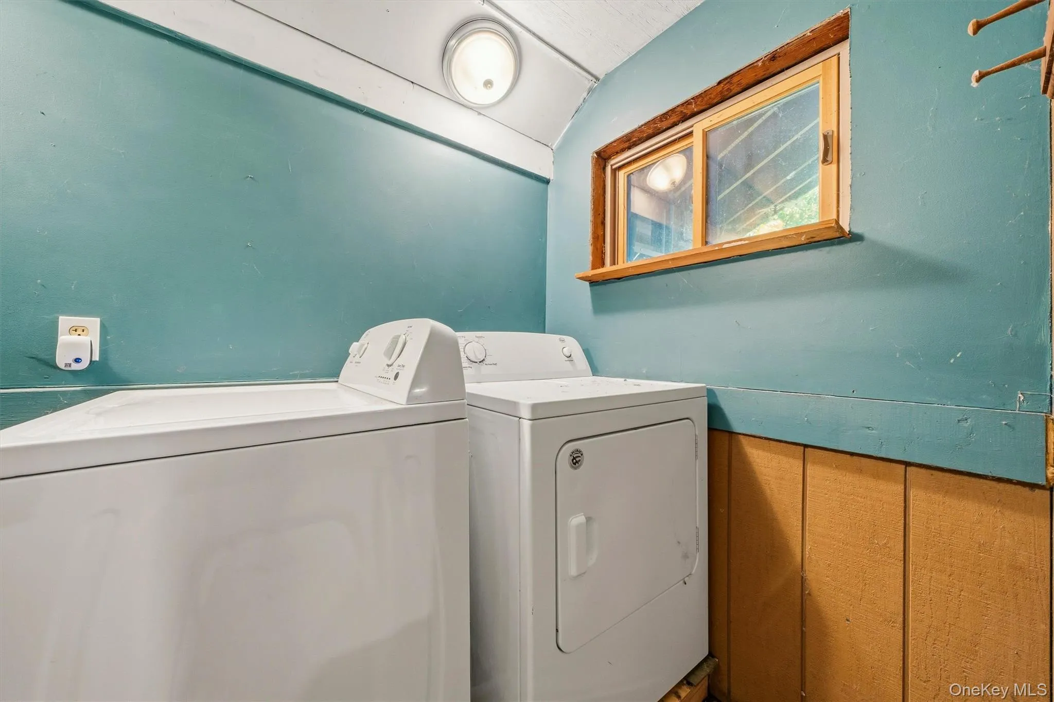 Laundry area with a window, wood-paneled wainscoting, and a wall-mounted light fixture Laundry area with a window, wood-paneled wainscoting, and a wall-mounted light fixture