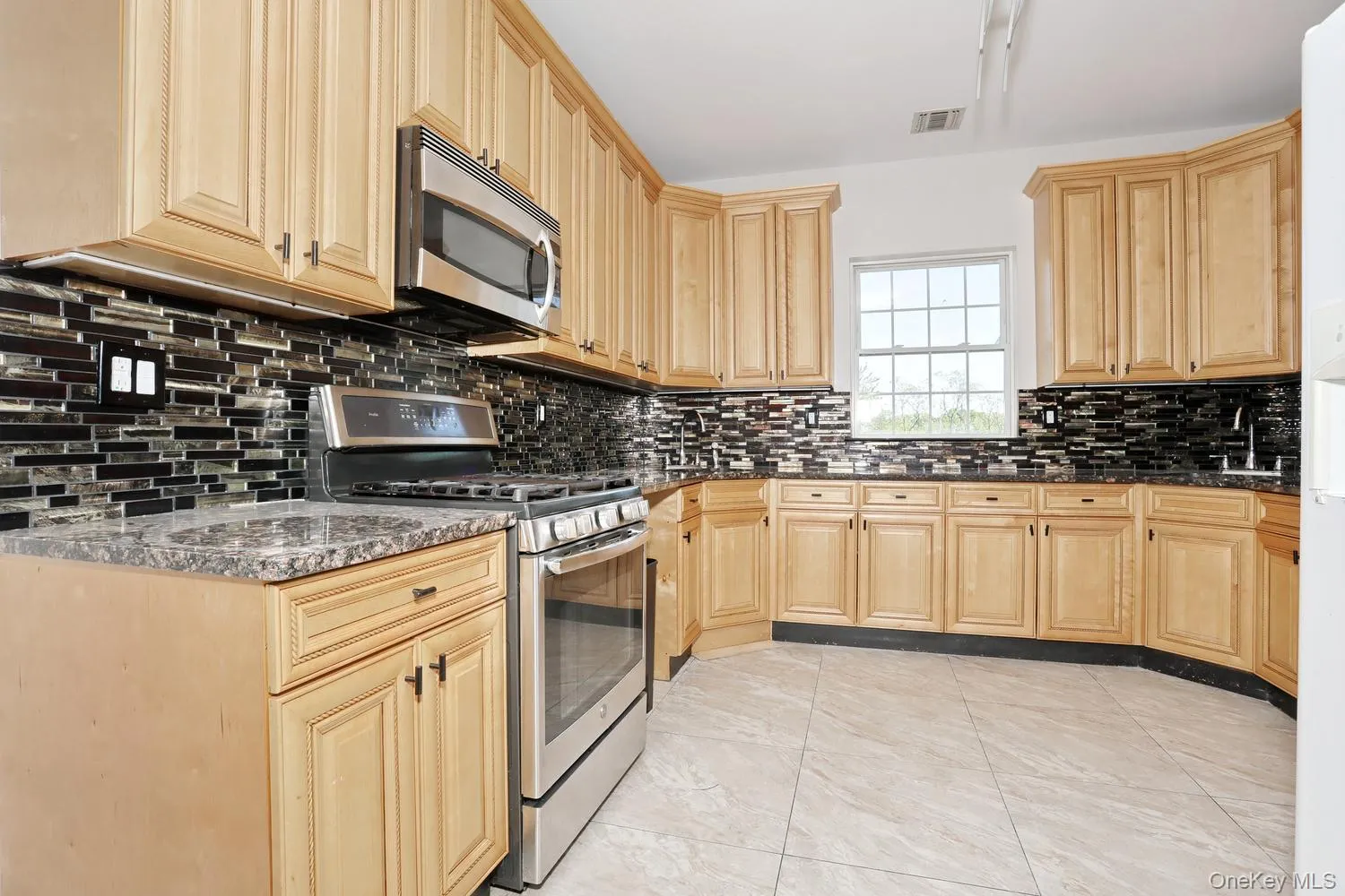 Spacious kitchen featuring extensive light wood cabinetry, a mosaic tile backsplash, and stone-finish countertops Spacious kitchen featuring extensive light wood cabinetry, a mosaic tile backsplash, and stone-finish countertops