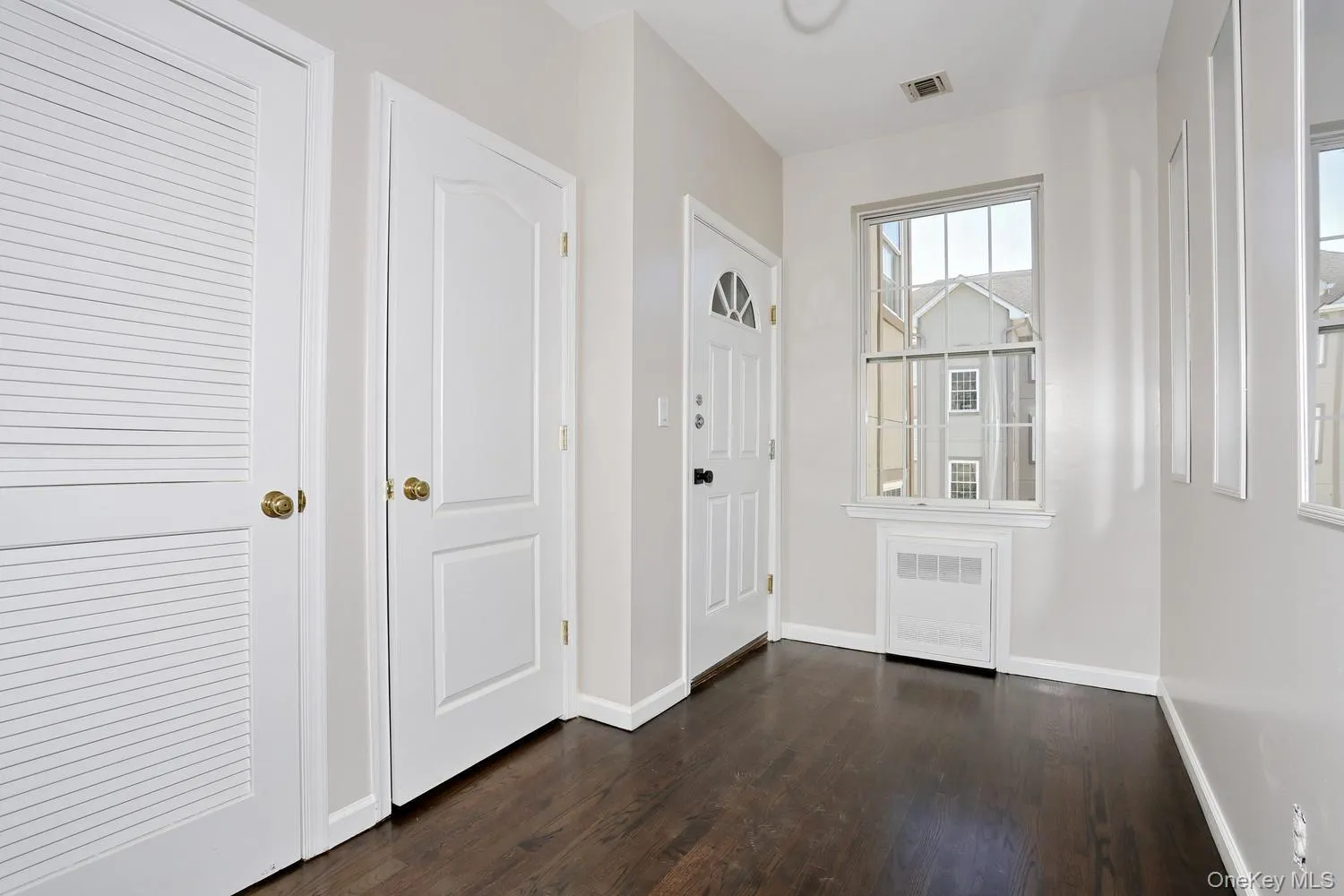 Entryway featuring wood-finish flooring, a paneled entry door with an arched window insert, and a double-hung window Entryway featuring wood-finish flooring, a paneled entry door with an arched window insert, and a double-hung window