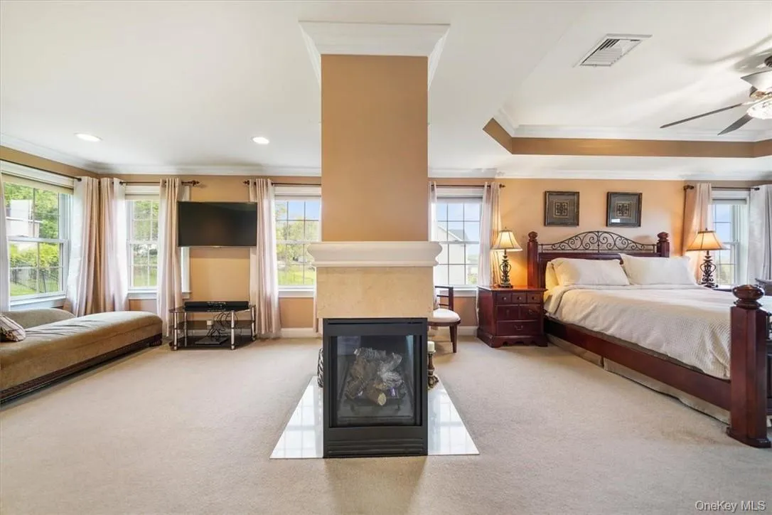 Bedroom with a multi sided fireplace, ornamental molding, a tray ceiling, carpet floors, and ceiling fan Bedroom with a multi sided fireplace, ornamental molding, a tray ceiling, carpet floors, and ceiling fan