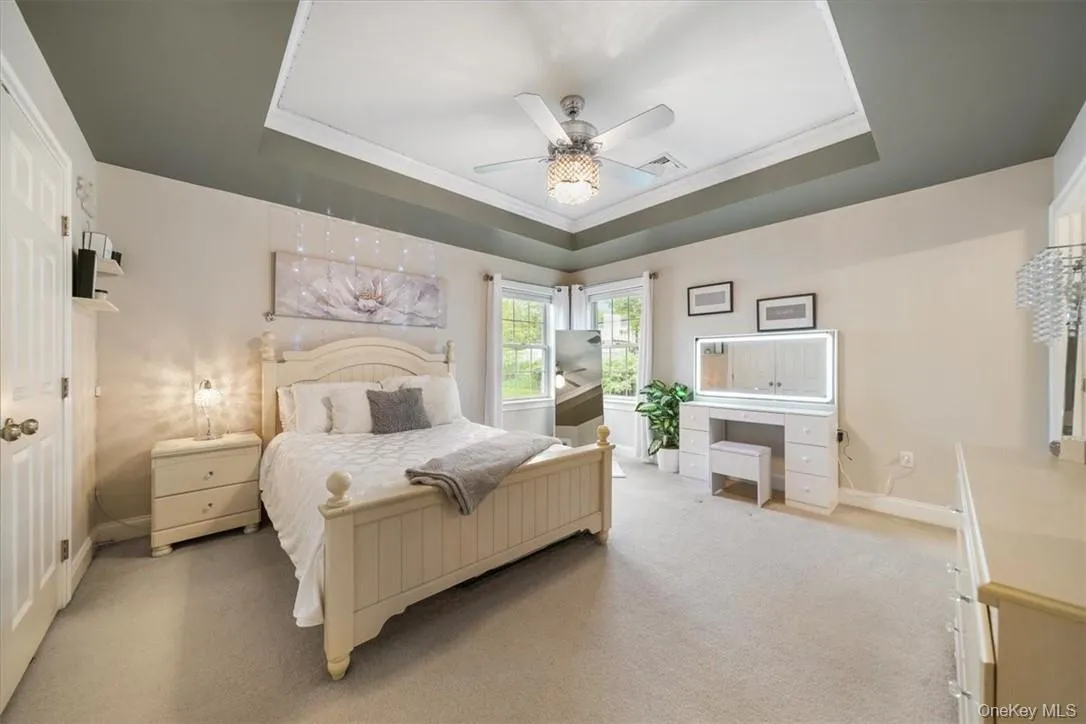 Carpeted bedroom featuring ceiling fan and a raised ceiling Carpeted bedroom featuring ceiling fan and a raised ceiling
