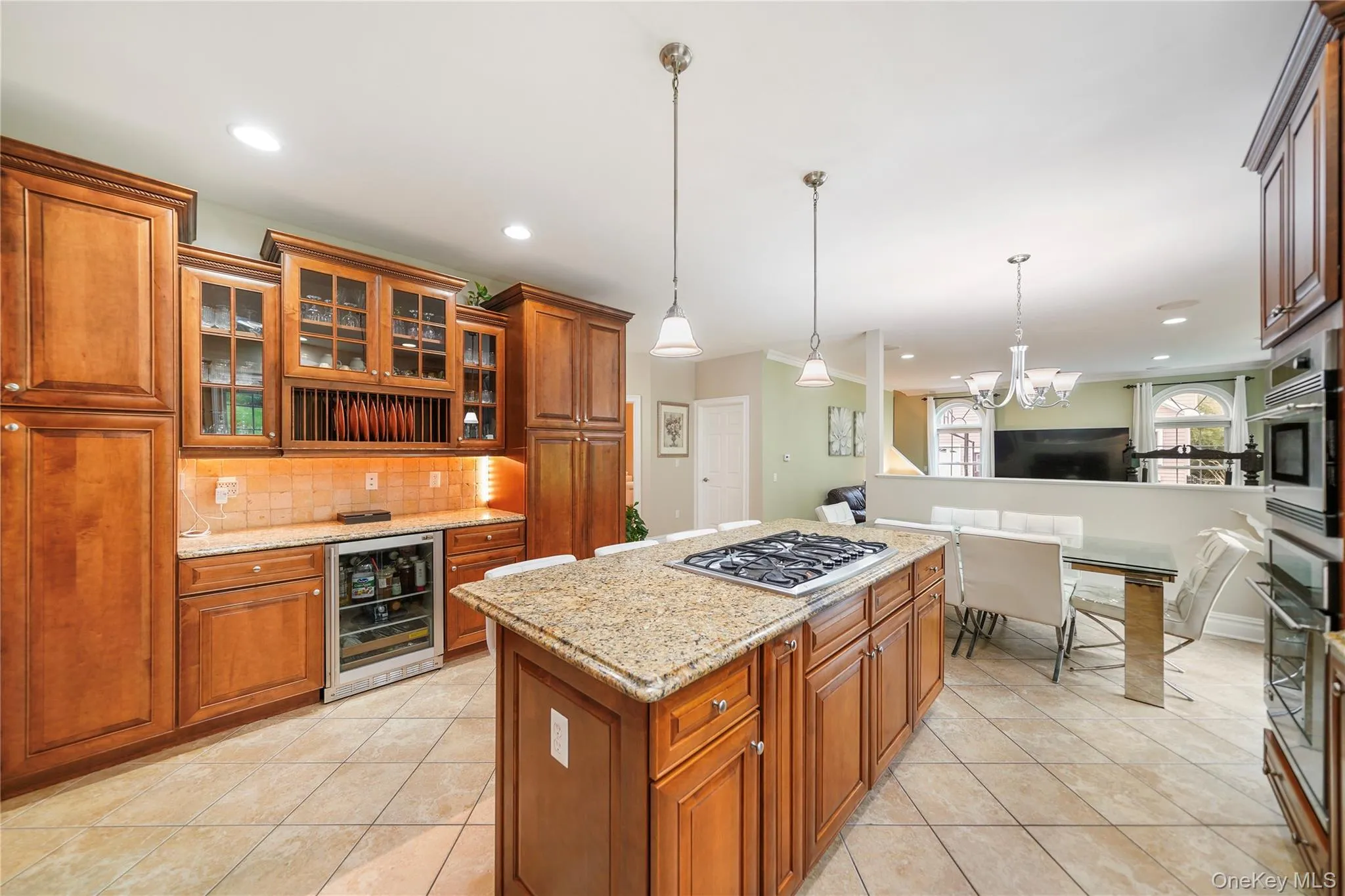Open-concept kitchen featuring an island with a gas cooktop, granite countertops, tile flooring, rich wood cabinetry, and recessed lighting Open-concept kitchen featuring an island with a gas cooktop, granite countertops, tile flooring, rich wood cabinetry, and recessed lighting