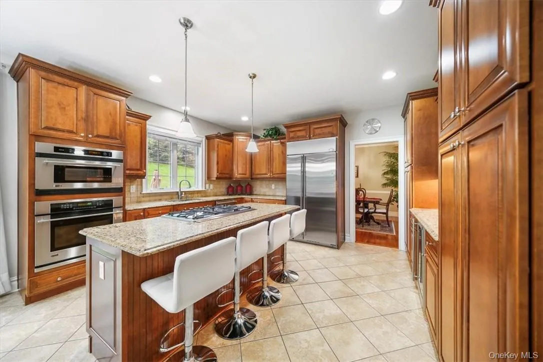 Kitchen with tasteful backsplash, pendant lighting, a kitchen island, light tile floors, and appliances with stainless steel finishes Kitchen with tasteful backsplash, pendant lighting, a kitchen island, light tile floors, and appliances with stainless steel finishes