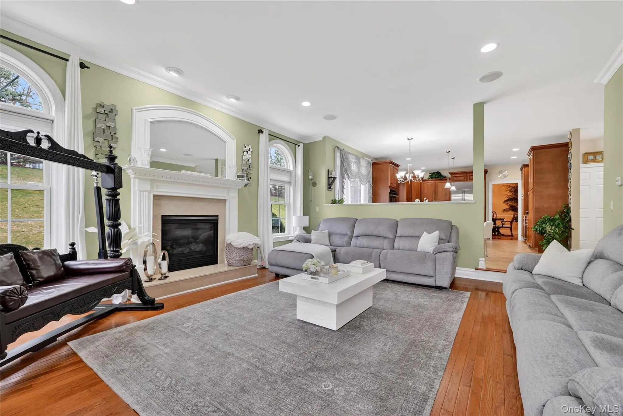 Spacious living area featuring rich wood flooring, a fireplace with a detailed mantel, and arched windows Spacious living area featuring rich wood flooring, a fireplace with a detailed mantel, and arched windows
