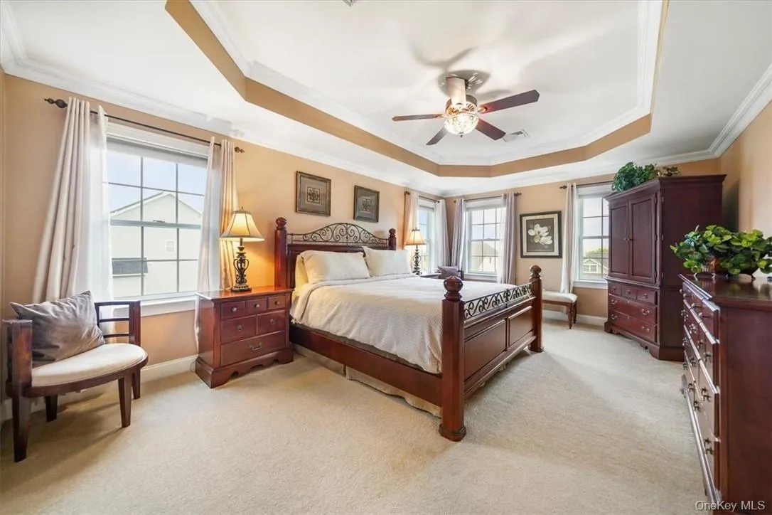 Bedroom with light colored carpet, ceiling fan, a tray ceiling, and crown molding with fireplace Bedroom with light colored carpet, ceiling fan, a tray ceiling, and crown molding with fireplace