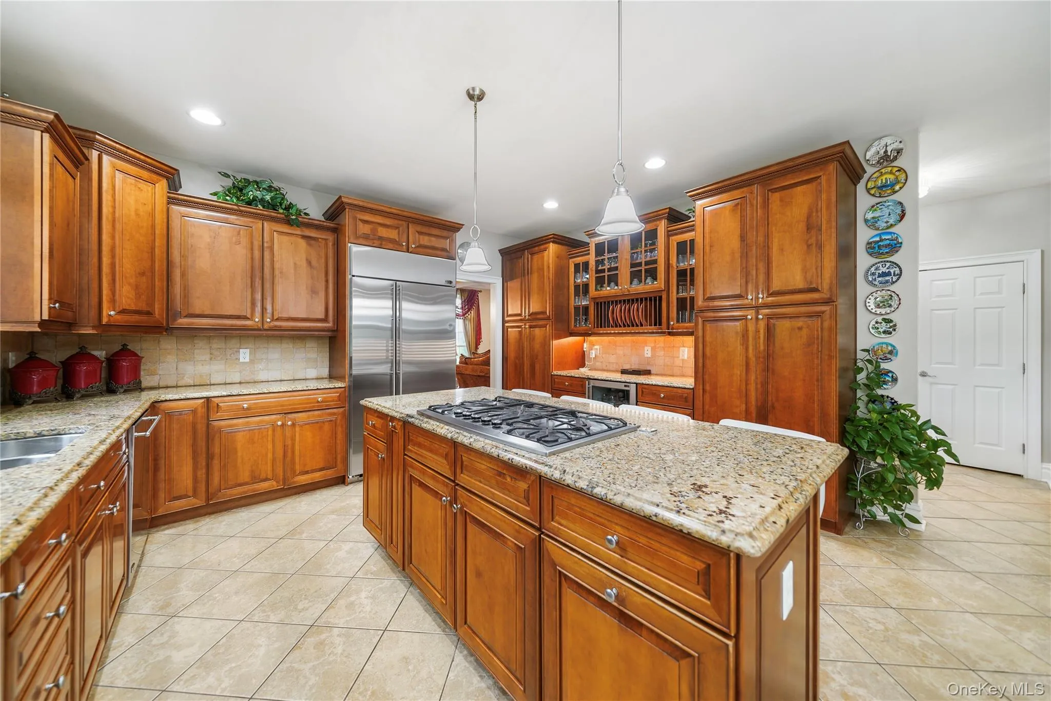 Gourmet kitchen featuring a central island with a gas cooktop, granite countertops, tile flooring, rich wood cabinetry, and stainless steel appliances Gourmet kitchen featuring a central island with a gas cooktop, granite countertops, tile flooring, rich wood cabinetry, and stainless steel appliances