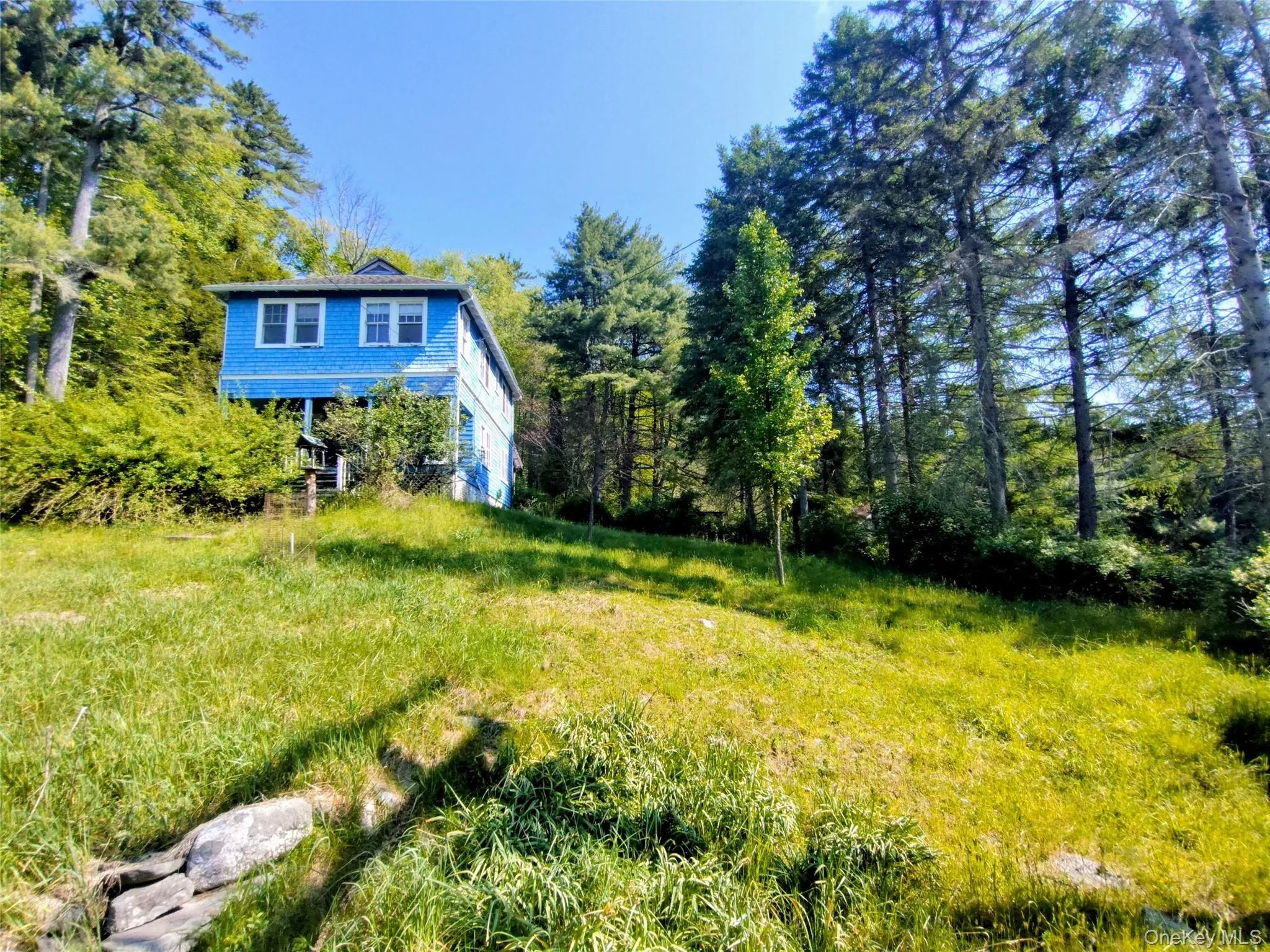 Two-story blue residence surrounded by mature trees and natural landscaping Two-story blue residence surrounded by mature trees and natural landscaping