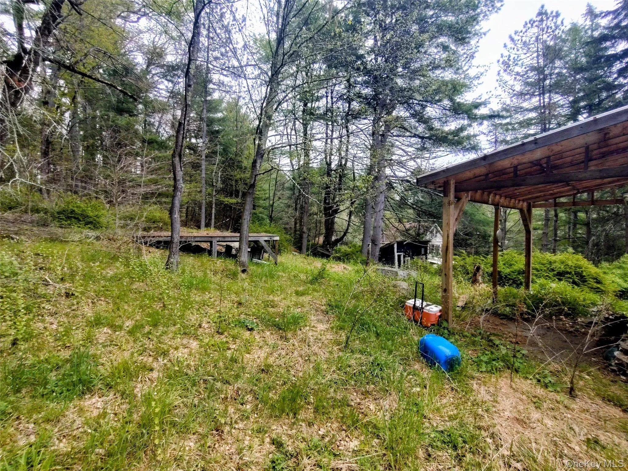 Wooded lot featuring an elevated wood platform and an open-sided shed with a metal roof and wood supports Wooded lot featuring an elevated wood platform and an open-sided shed with a metal roof and wood supports