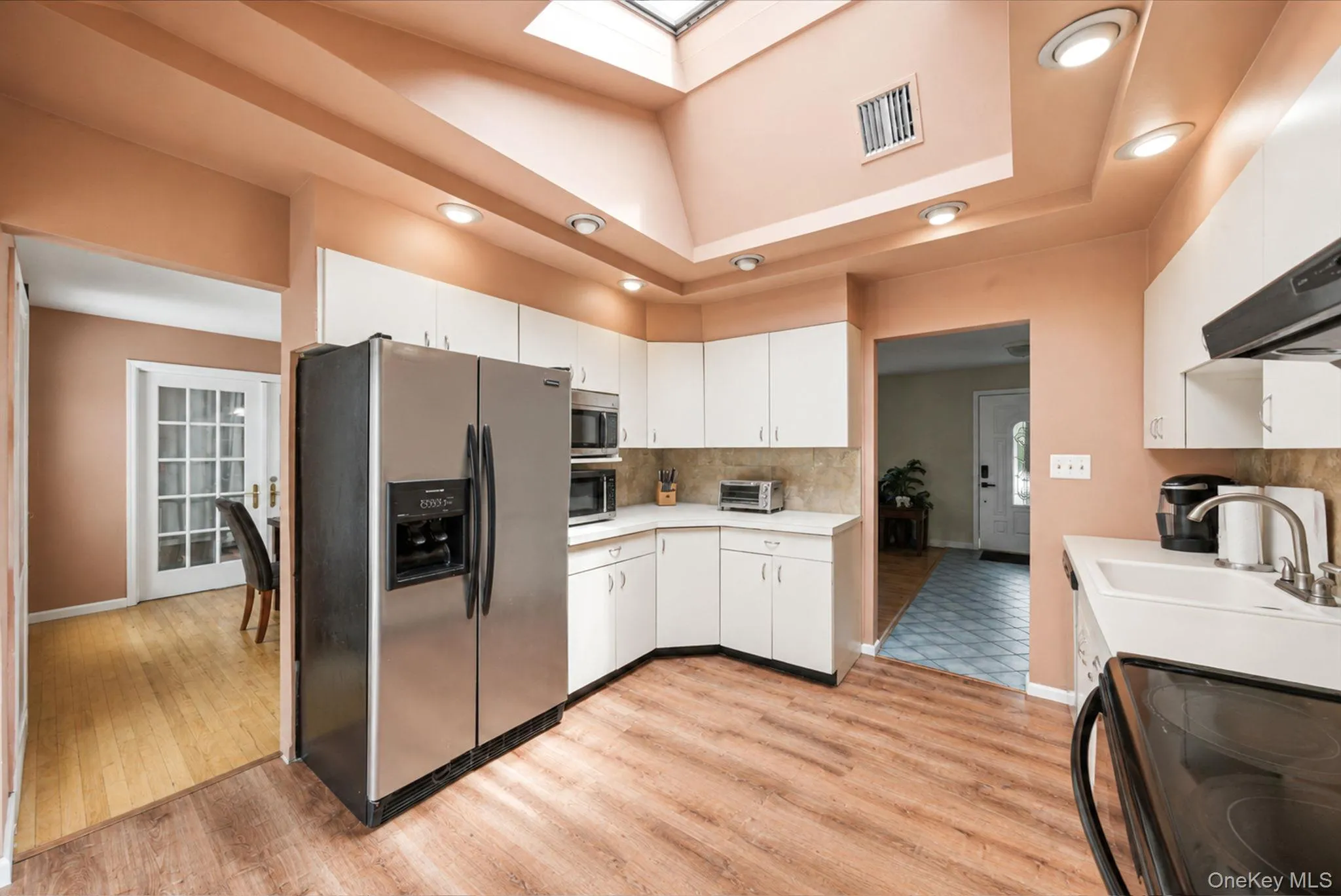 Kitchen featuring wood-finish flooring, white cabinetry, light countertops, and stainless steel appliances Trace Ceiling with Skylight Kitchen featuring wood-finish flooring, white cabinetry, light countertops, and stainless steel appliances Trace Ceiling with Skylight
