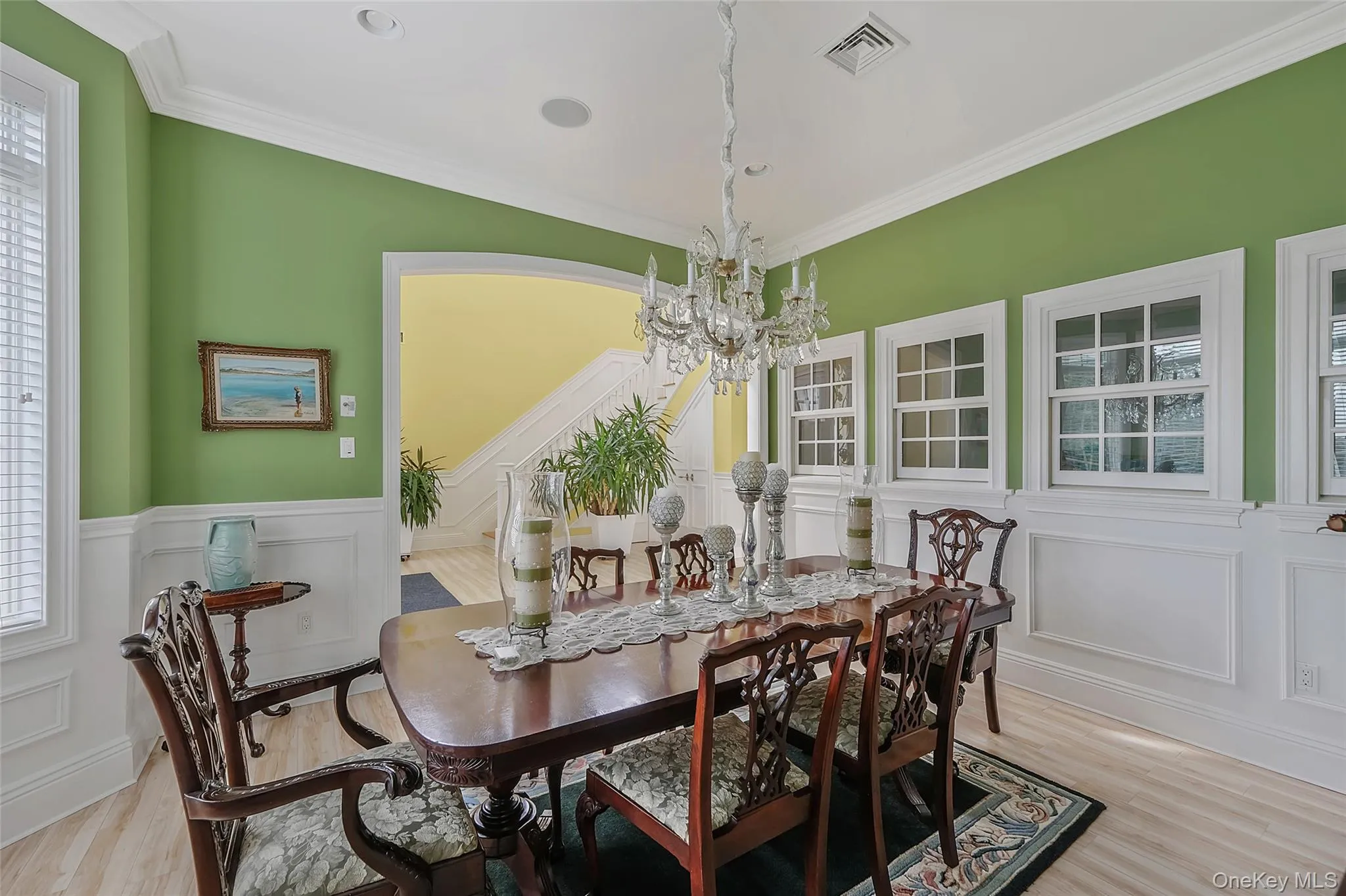 Dining space featuring a crystal chandelier, wood-finish flooring, white crown molding, white wainscoting, and multiple windows Dining space featuring a crystal chandelier, wood-finish flooring, white crown molding, white wainscoting, and multiple windows