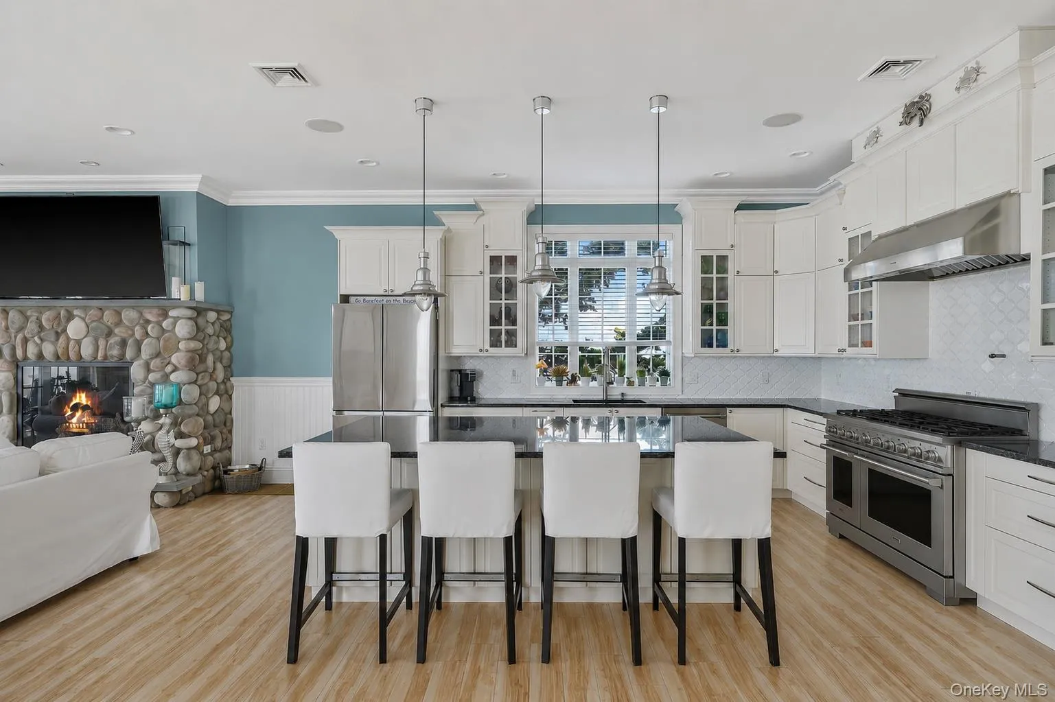 Open-concept kitchen featuring white cabinetry, a large kitchen island with pendant lighting, stainless steel appliances, and wood-finish flooring Open-concept kitchen featuring white cabinetry, a large kitchen island with pendant lighting, stainless steel appliances, and wood-finish flooring
