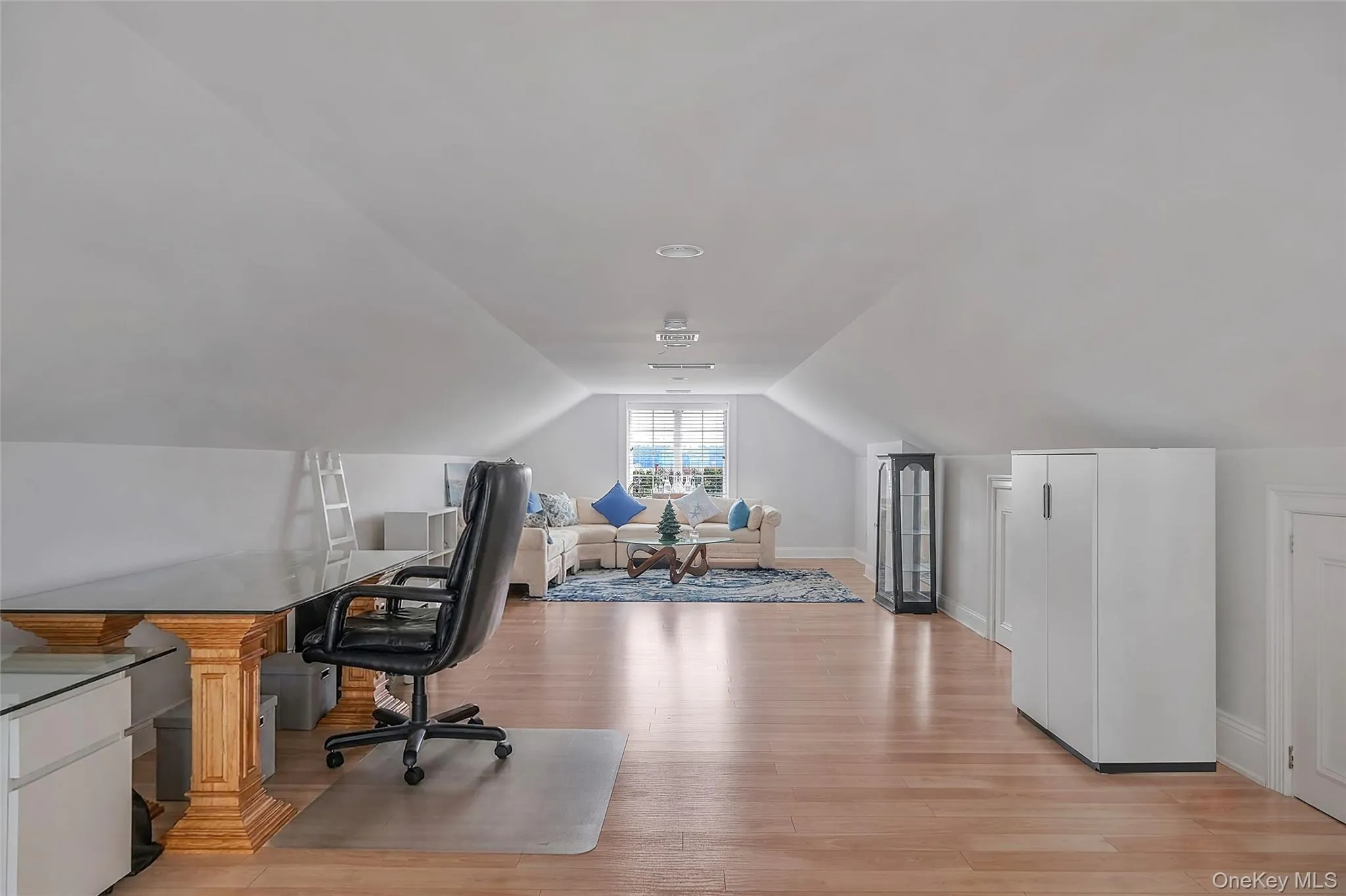 Spacious loft room featuring wood-finish flooring, recessed lighting, and a window providing natural light Spacious loft room featuring wood-finish flooring, recessed lighting, and a window providing natural light