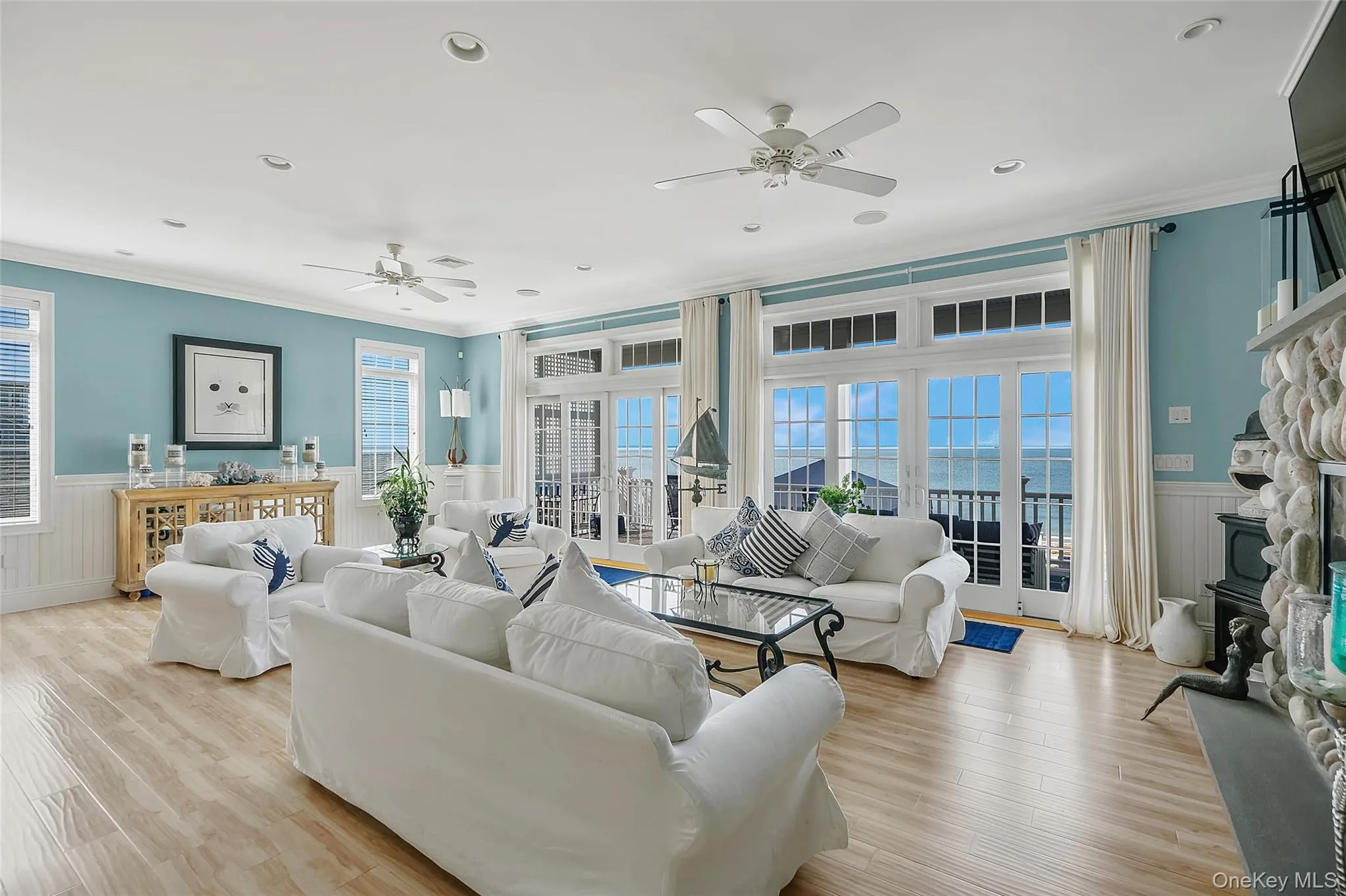 Spacious living area featuring wood-finish flooring, white paneled wainscoting, and large glass sliding doors opening to an exterior balcony Spacious living area featuring wood-finish flooring, white paneled wainscoting, and large glass sliding doors opening to an exterior balcony