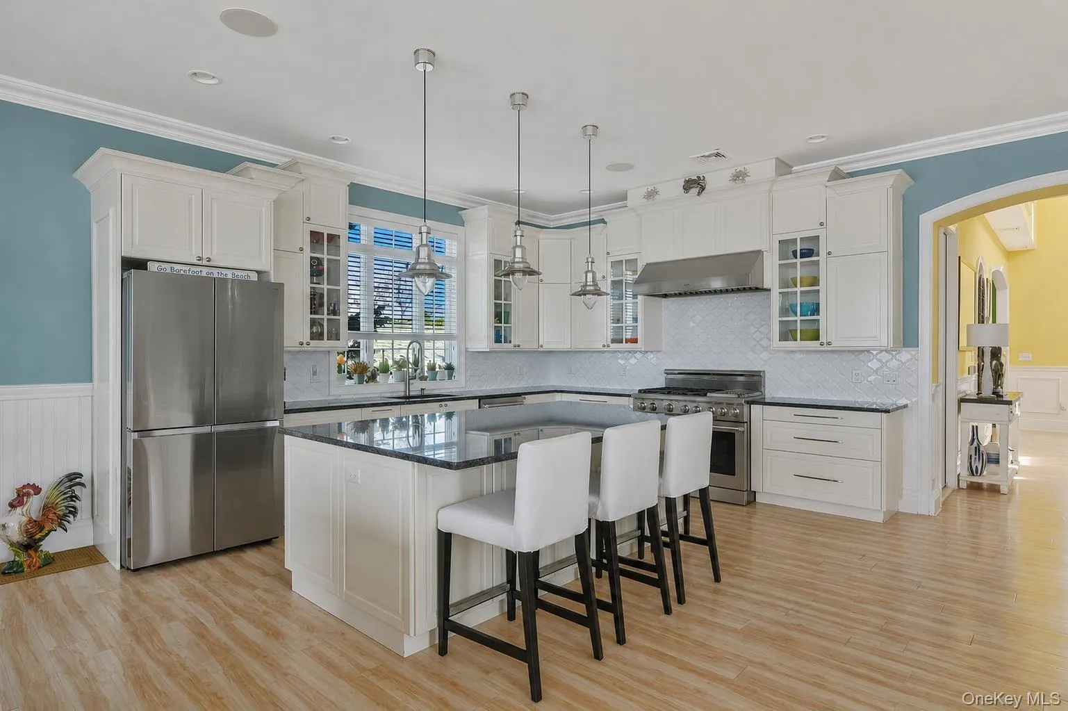 Well-appointed kitchen featuring white cabinetry, granite countertops, a large center island, stainless steel appliances, and wood-finish flooring Well-appointed kitchen featuring white cabinetry, granite countertops, a large center island, stainless steel appliances, and wood-finish flooring