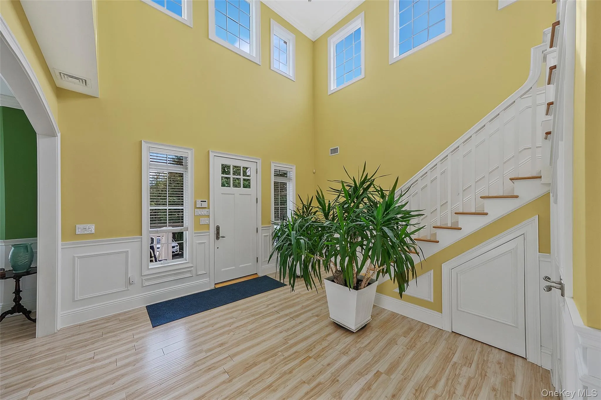 Two-story foyer featuring wood-finish flooring, wainscoting, and a white staircase with wood treads Two-story foyer featuring wood-finish flooring, wainscoting, and a white staircase with wood treads