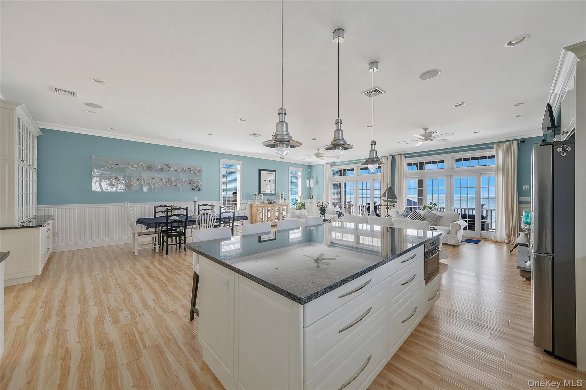 Spacious open-concept living area featuring an expansive kitchen island with a granite countertop, wood-finish flooring throughout, and a wall of glass-paneled doors with transom windows Spacious open-concept living area featuring an expansive kitchen island with a granite countertop, wood-finish flooring throughout, and a wall of glass-paneled doors with transom windows