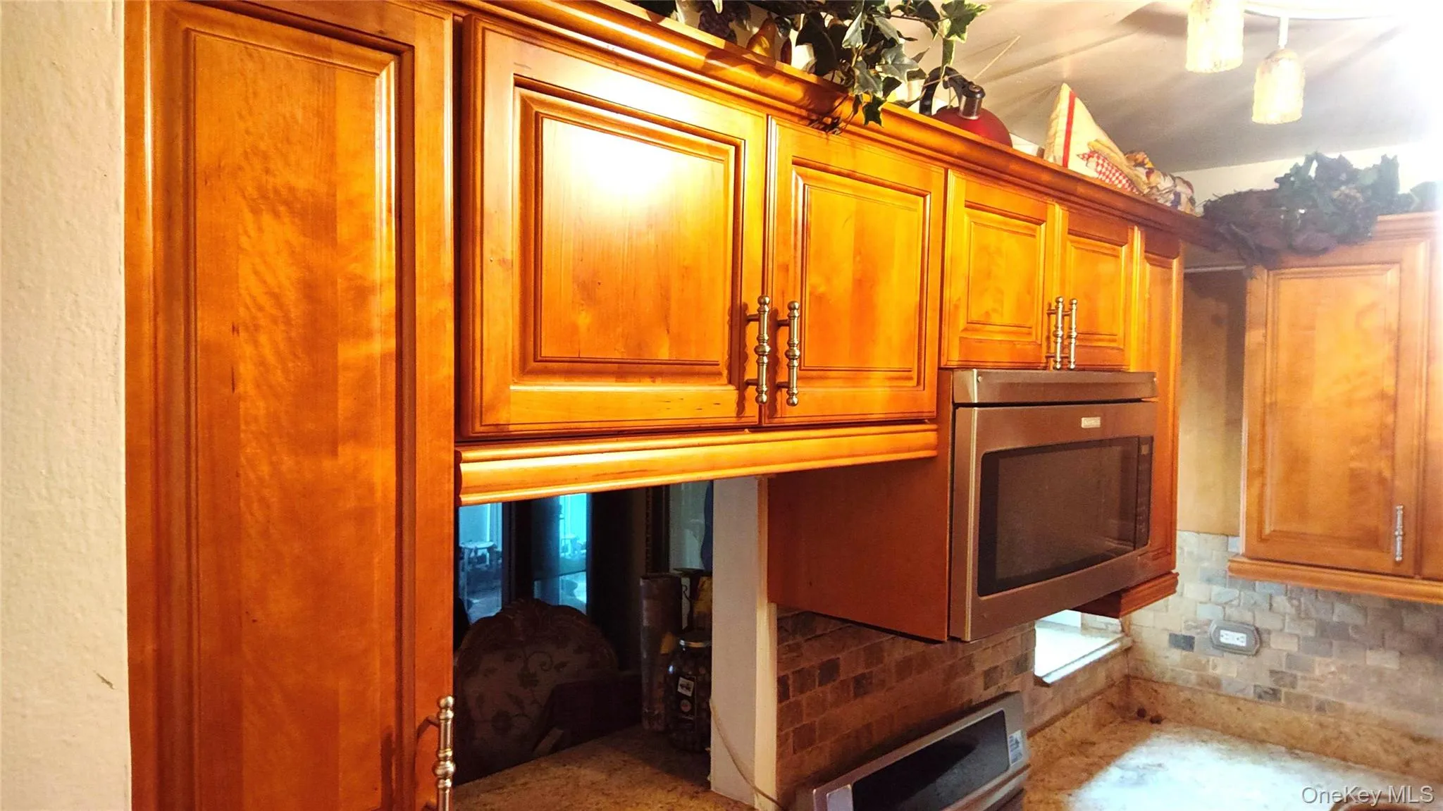Kitchen featuring upper cabinetry with panel doors and decorative hardware, a built-in stainless steel microwave, and stone tile backsplash Kitchen featuring upper cabinetry with panel doors and decorative hardware, a built-in stainless steel microwave, and stone tile backsplash