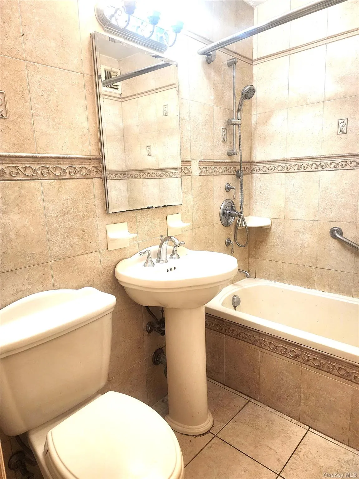 Full bathroom featuring floor-to-ceiling ceramic tile, a pedestal sink, and a bathtub with an integrated shower Full bathroom featuring floor-to-ceiling ceramic tile, a pedestal sink, and a bathtub with an integrated shower