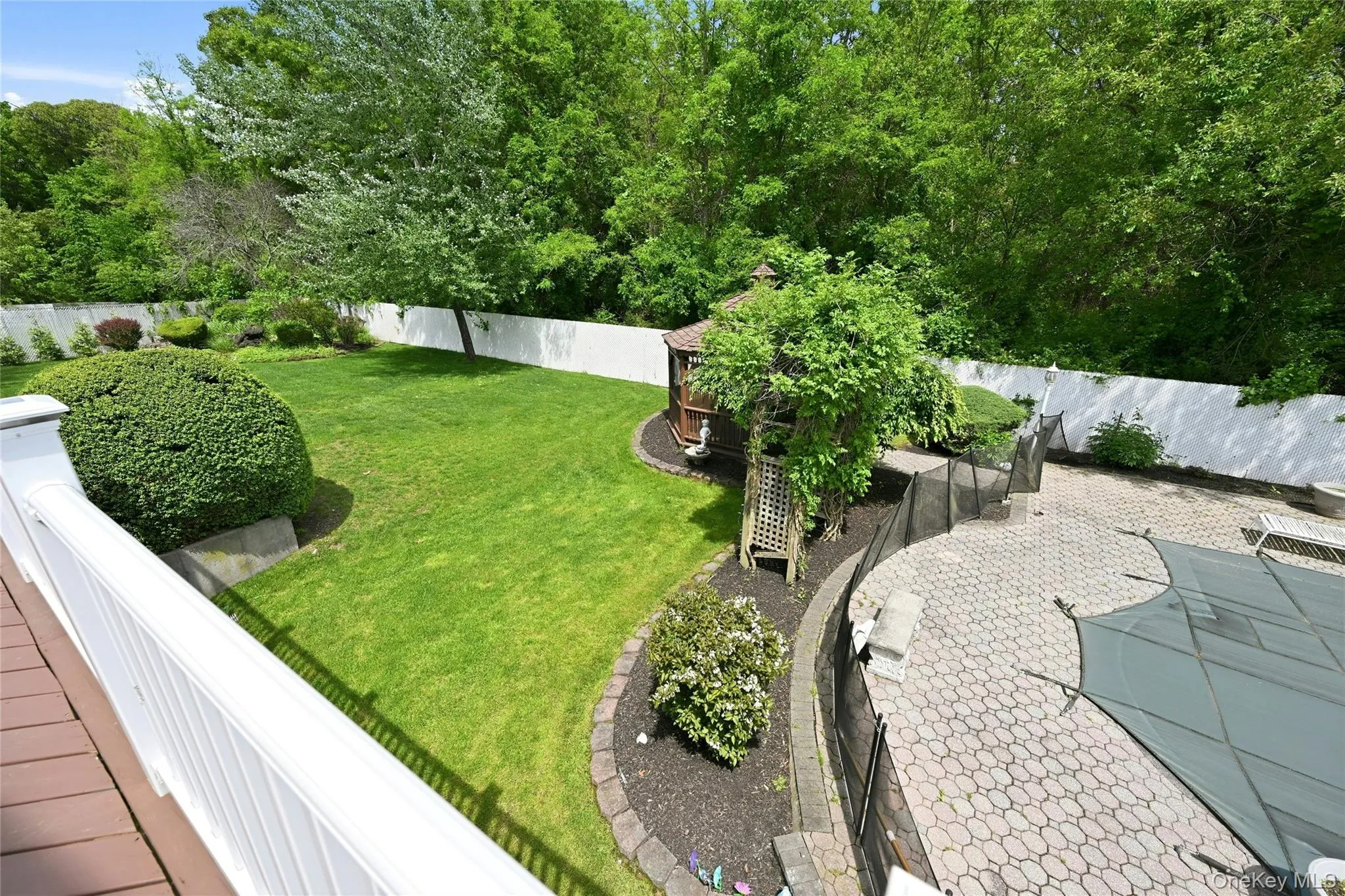 Expansive backyard featuring a lush lawn, mature perimeter trees, a white privacy fence, a paved patio, and a covered pool area Expansive backyard featuring a lush lawn, mature perimeter trees, a white privacy fence, a paved patio, and a covered pool area