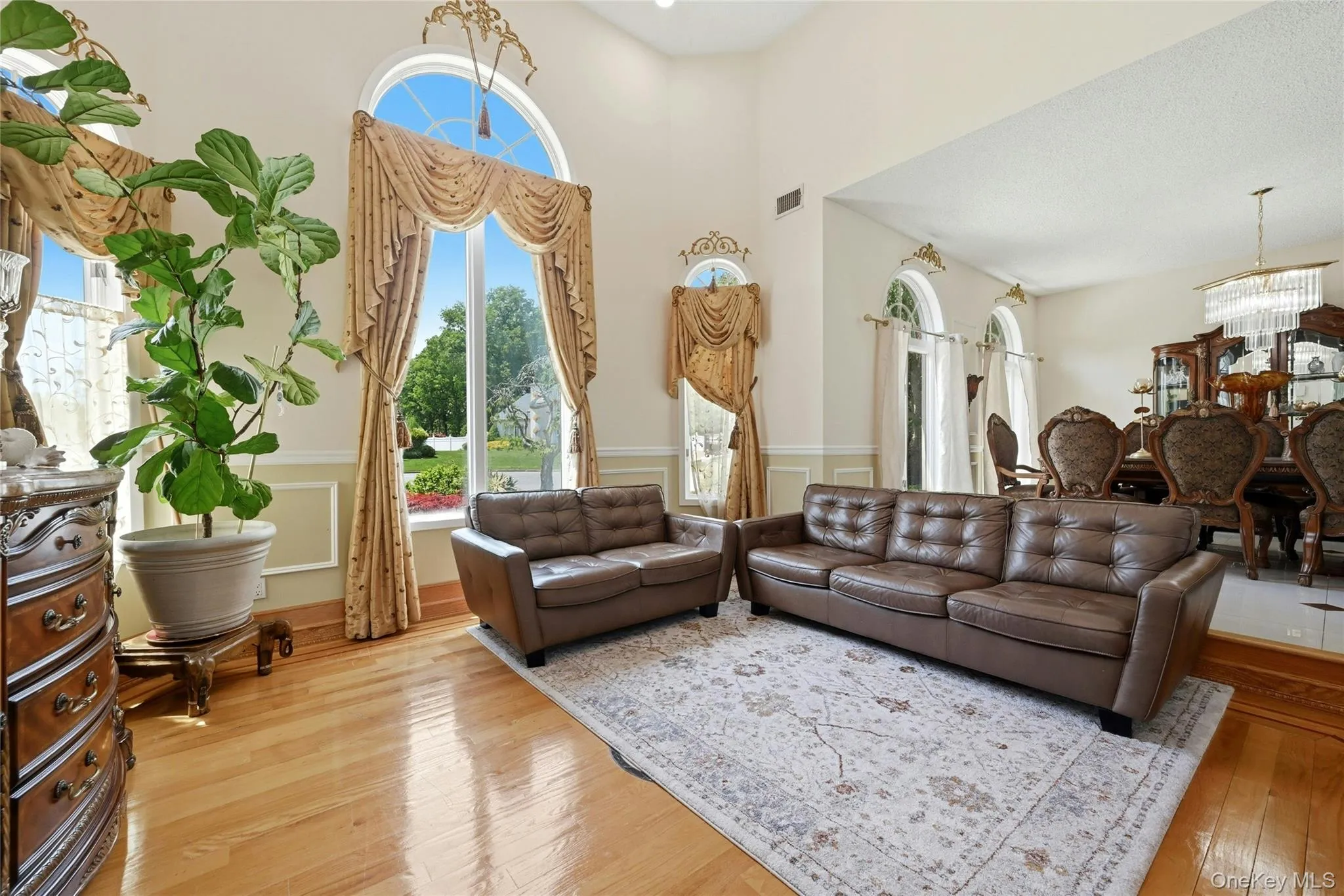 Spacious living area featuring polished wood-finish flooring, tall vaulted ceilings, and large arched windows Spacious living area featuring polished wood-finish flooring, tall vaulted ceilings, and large arched windows