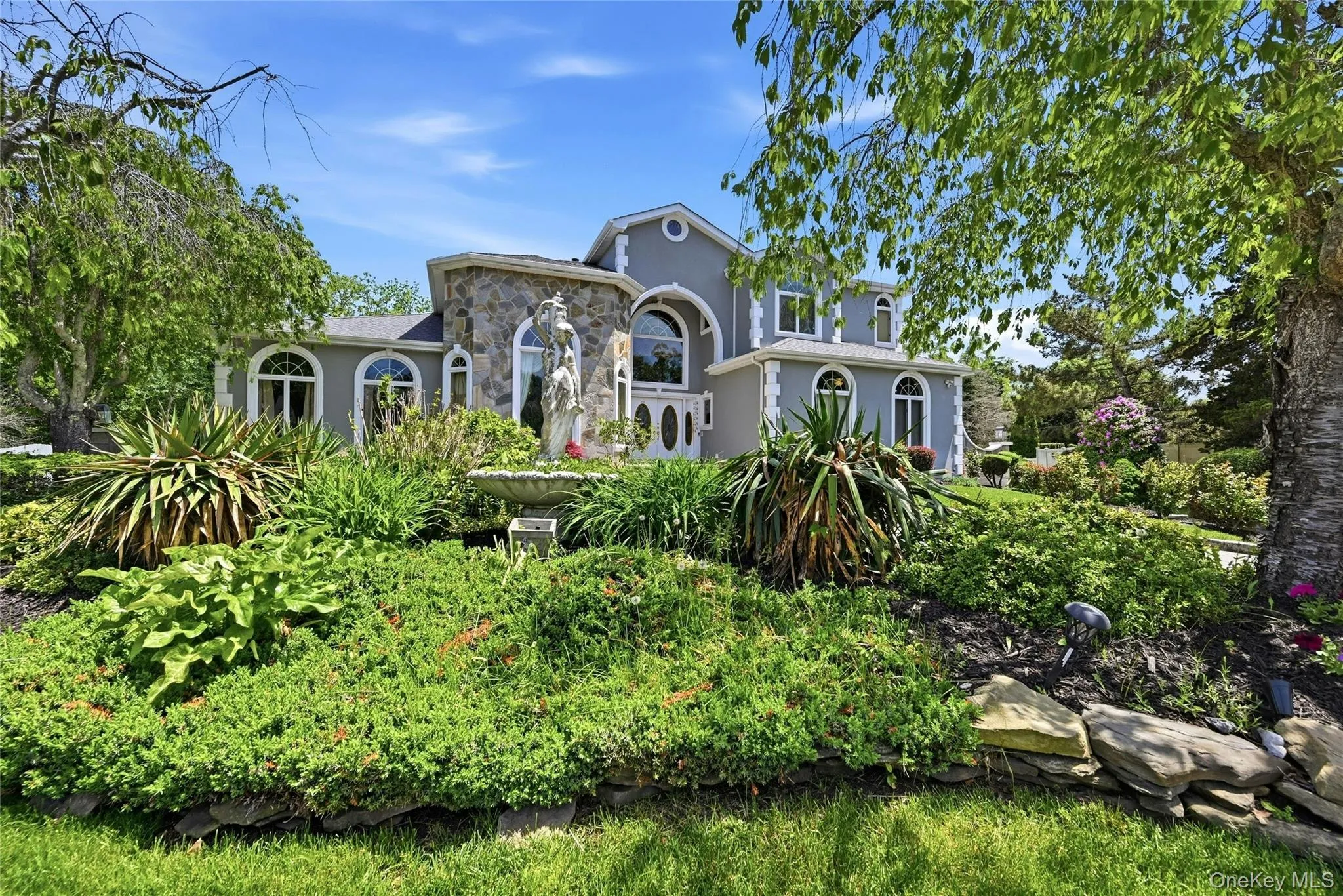 Stone facade exterior with arched windows, a grand double-door entry, and a tiered garden featuring a central fountain Stone facade exterior with arched windows, a grand double-door entry, and a tiered garden featuring a central fountain