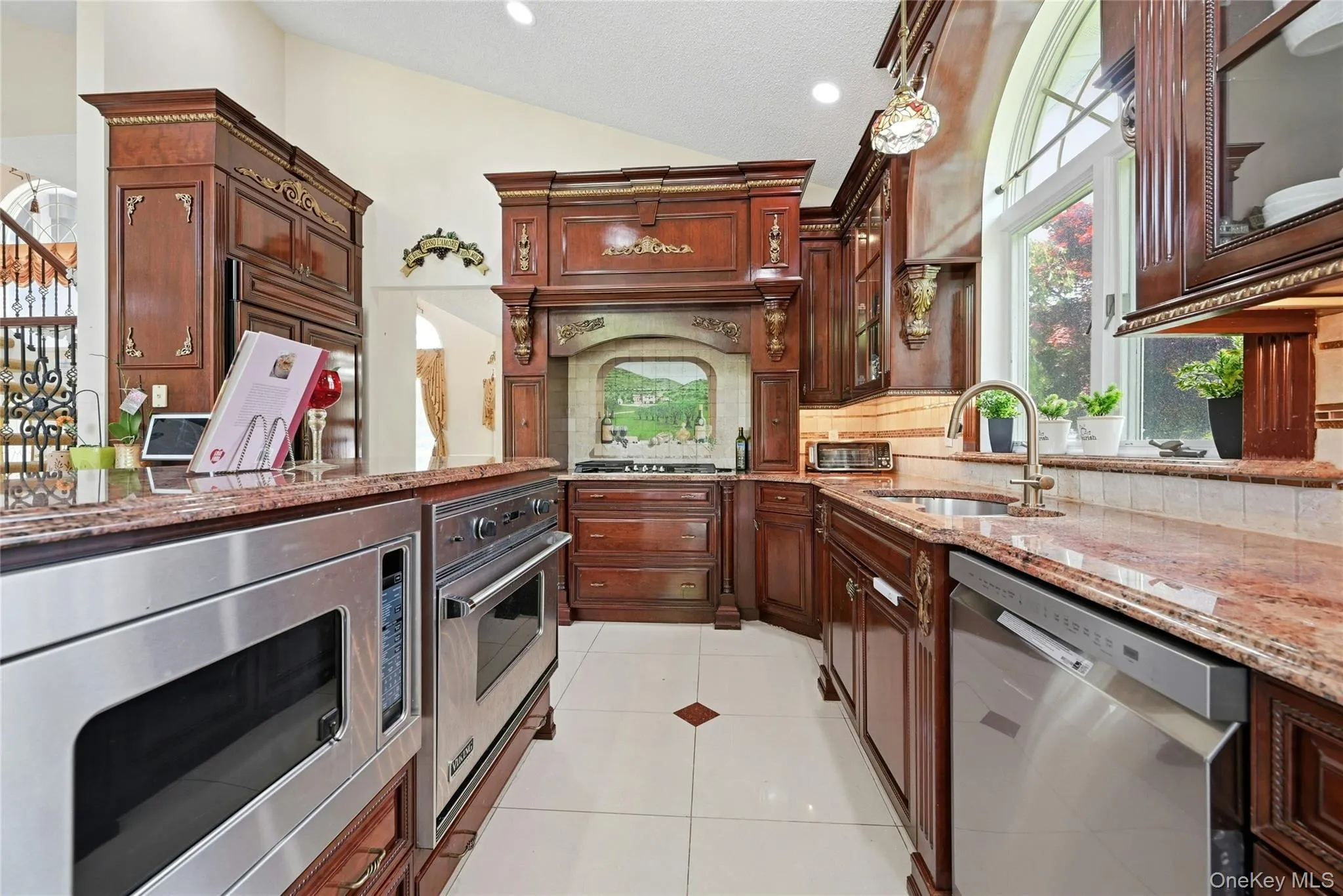 Kitchen featuring rich wood cabinetry, stainless steel appliances, granite countertops, and a large arched window Kitchen featuring rich wood cabinetry, stainless steel appliances, granite countertops, and a large arched window