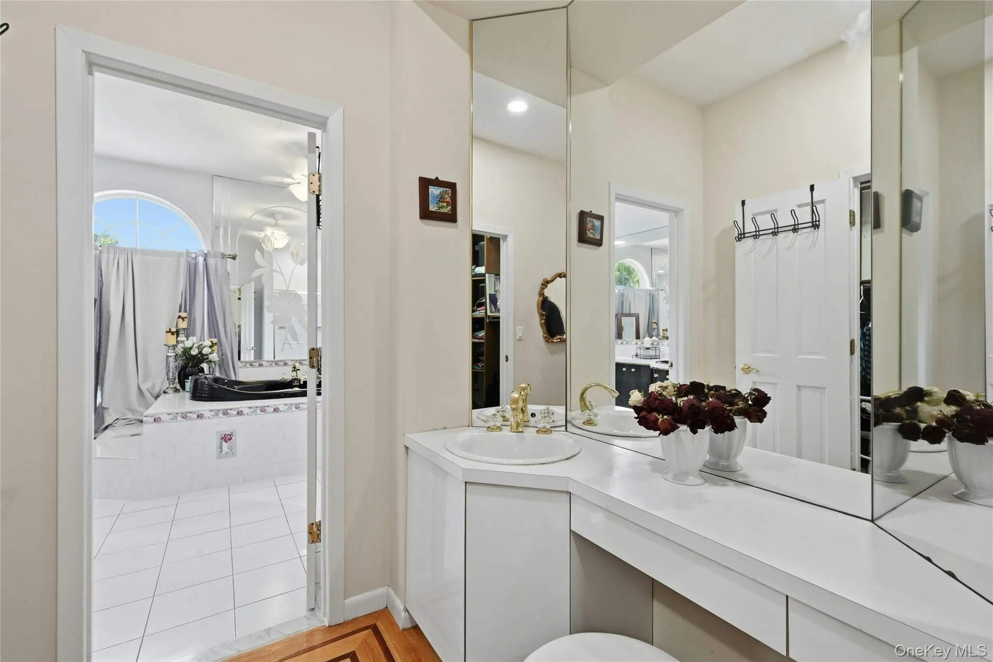 Integrated vanity area featuring a single basin sink with gold-tone fixtures, expansive wall-mounted mirrors, and ample counter space Integrated vanity area featuring a single basin sink with gold-tone fixtures, expansive wall-mounted mirrors, and ample counter space