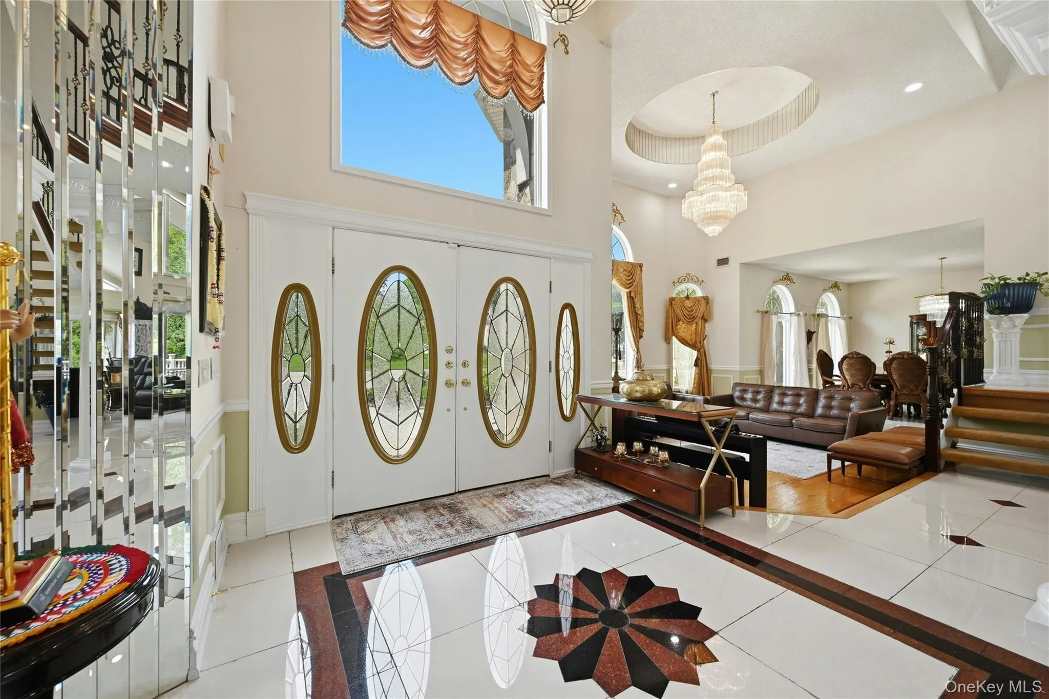 Grand foyer featuring double entry doors with decorative oval glass inserts, a two-story ceiling, and a large chandelier Grand foyer featuring double entry doors with decorative oval glass inserts, a two-story ceiling, and a large chandelier