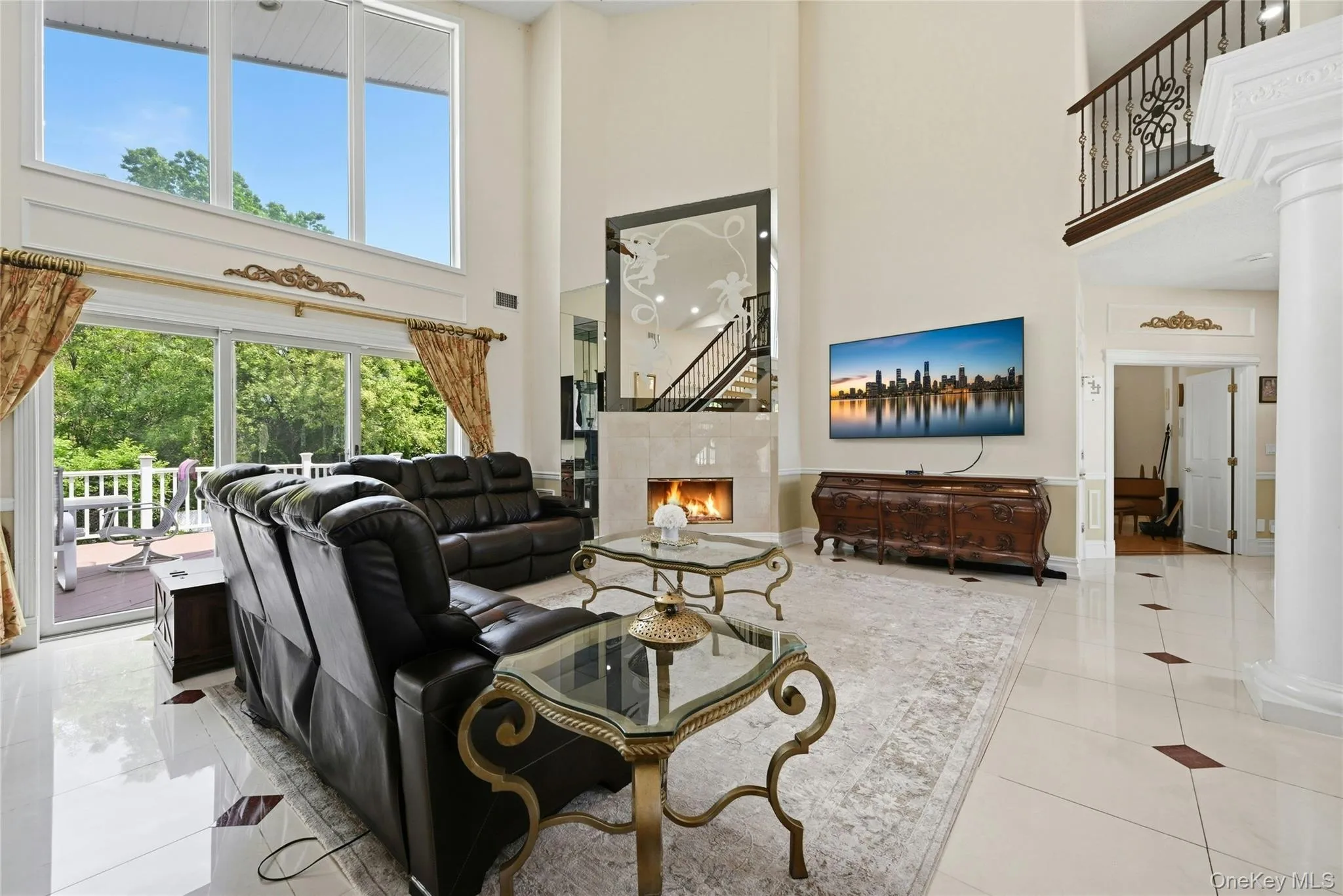 Two-story living area featuring a fireplace, tall windows, sliding glass doors to an outdoor deck, and light-toned tile flooring Two-story living area featuring a fireplace, tall windows, sliding glass doors to an outdoor deck, and light-toned tile flooring