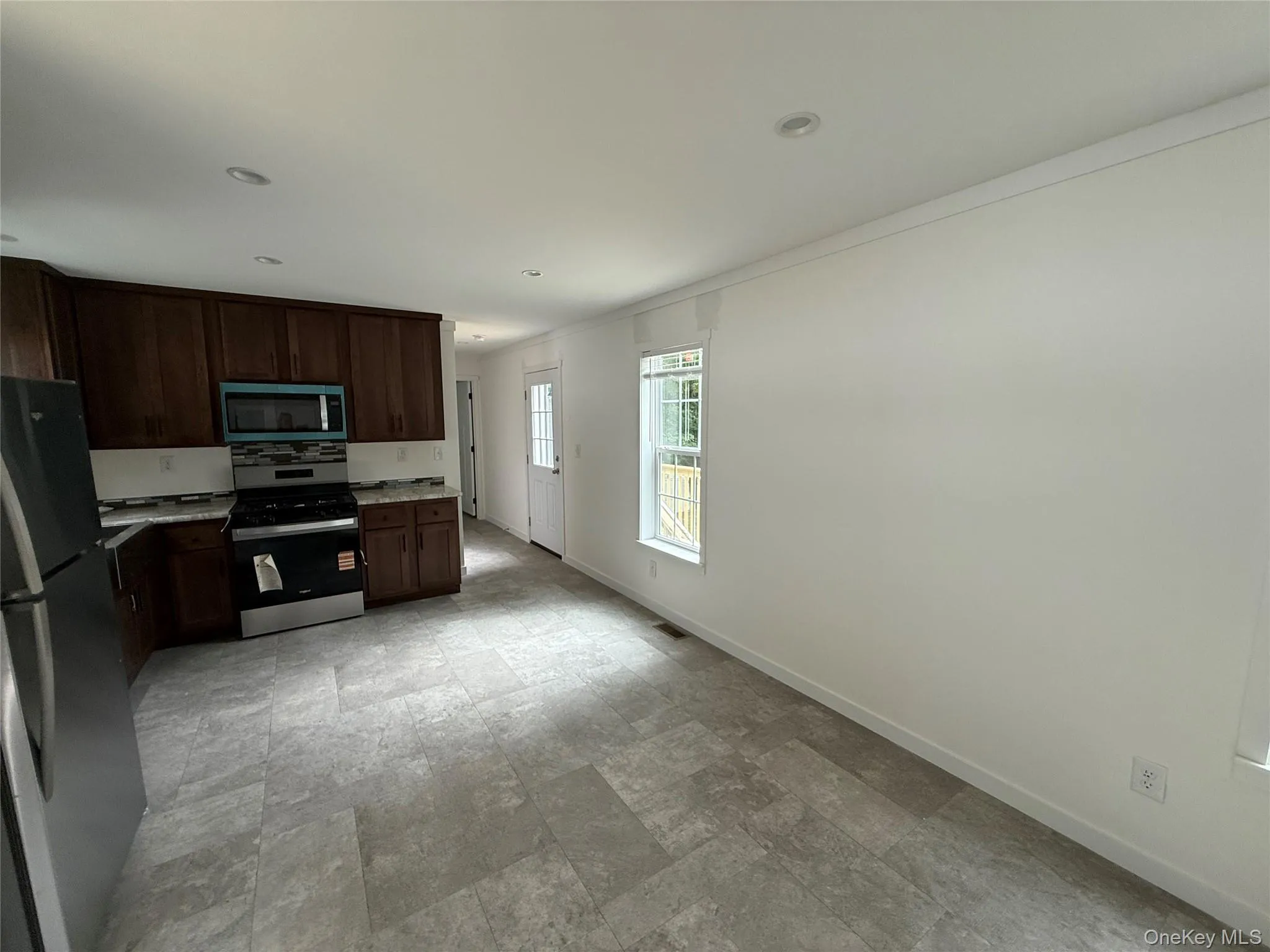 Kitchen featuring appliances with stainless steel finishes, dark brown cabinets, stone finish flooring, ornamental molding, and recessed lighting Kitchen featuring appliances with stainless steel finishes, dark brown cabinets, stone finish flooring, ornamental molding, and recessed lighting