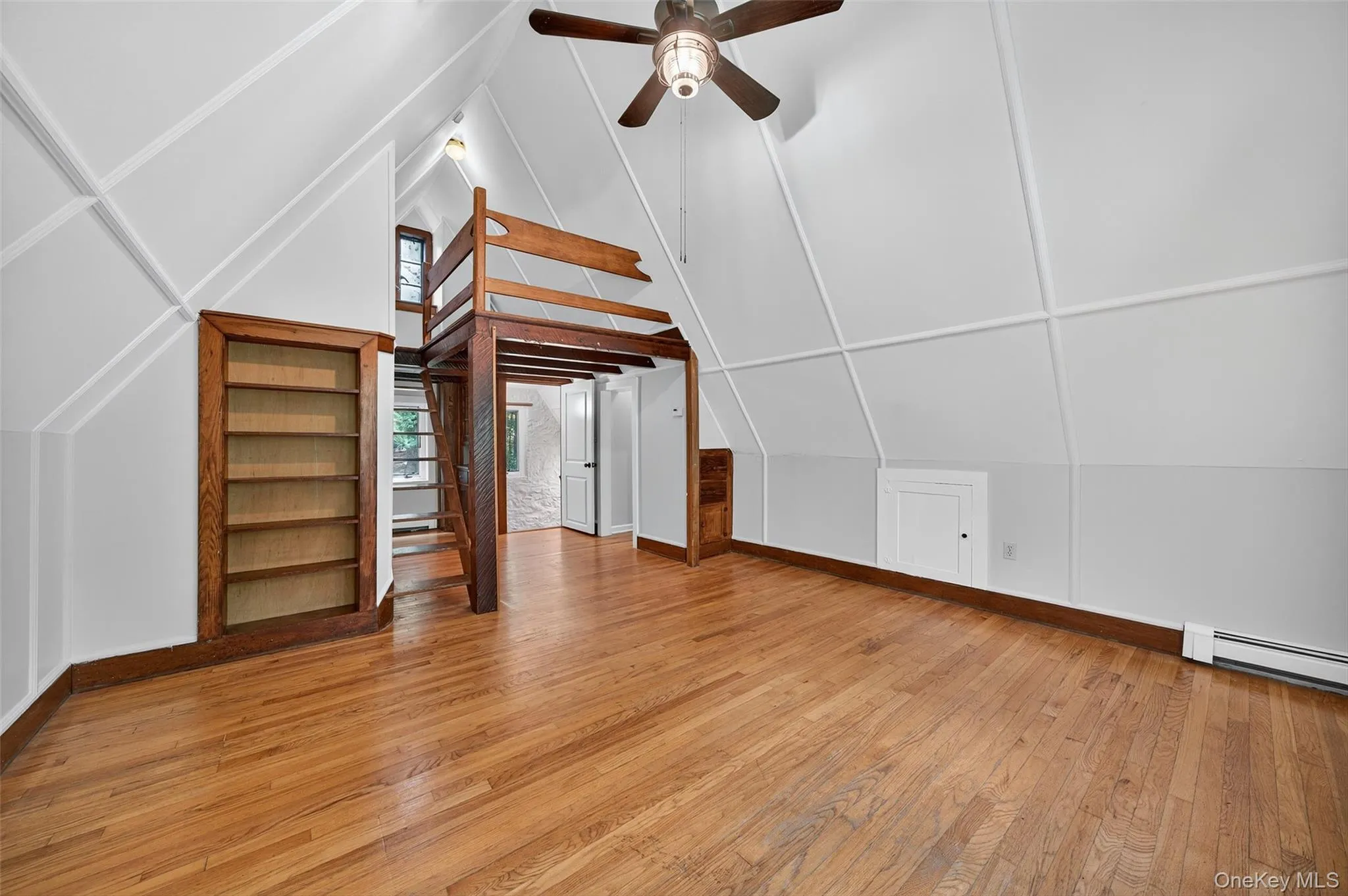 Additional living space with light wood finished floors, built-in shelving, vaulted ceiling, and a ceiling fan Additional living space with light wood finished floors, built-in shelving, vaulted ceiling, and a ceiling fan
