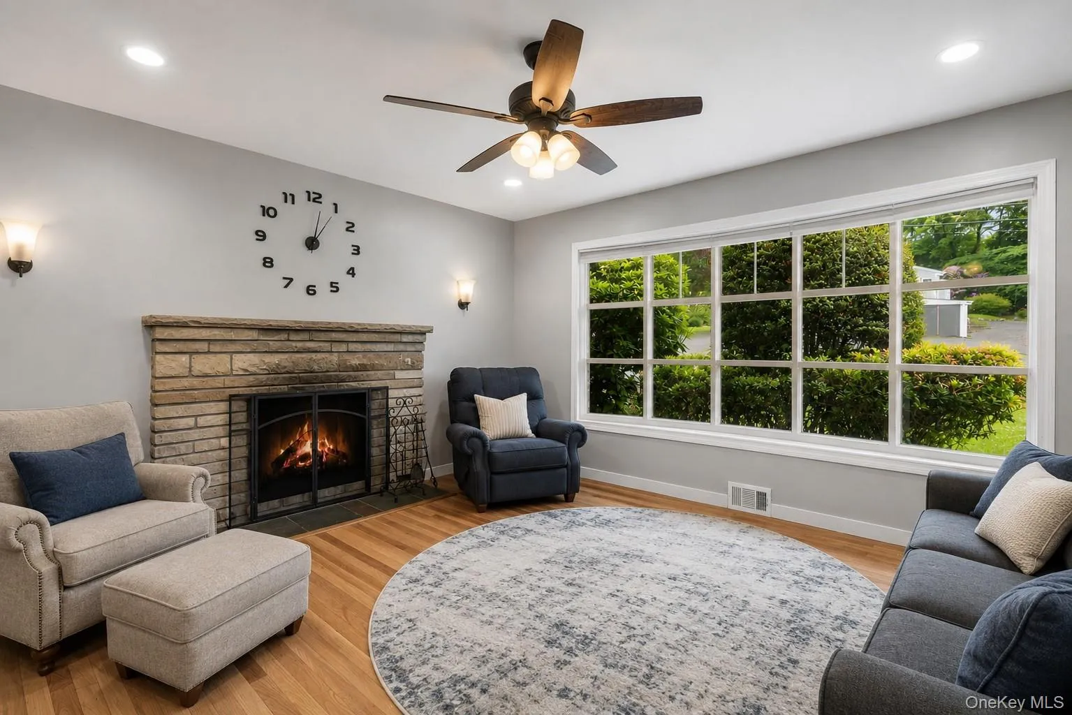 Living room featuring a stone-clad fireplace, wood-finish flooring, and a ceiling fan Living room featuring a stone-clad fireplace, wood-finish flooring, and a ceiling fan