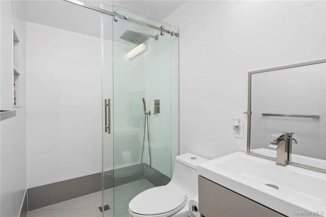 Bathroom featuring vanity, tile walls, toilet, and an enclosed shower Bathroom featuring vanity, tile walls, toilet, and an enclosed shower