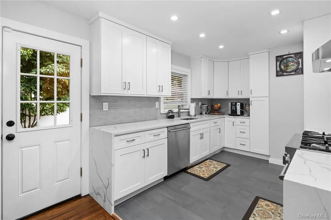 Kitchen with dishwasher, tasteful backsplash, sink, white cabinetry, and light stone countertops Kitchen with dishwasher, tasteful backsplash, sink, white cabinetry, and light stone countertops