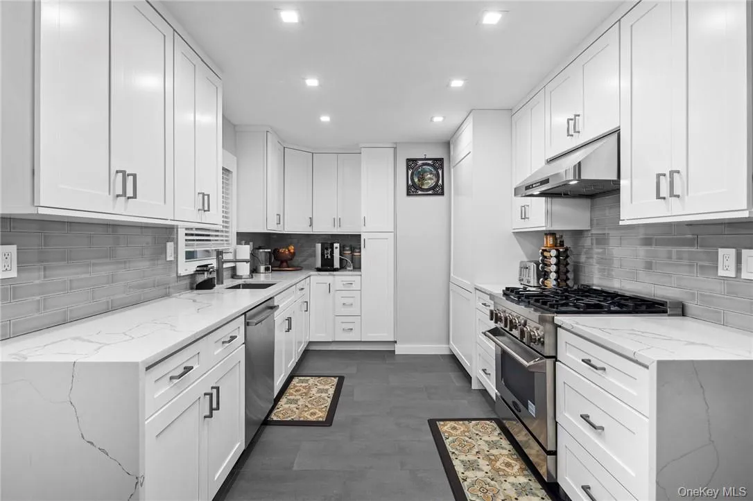 Kitchen featuring backsplash, white cabinetry, stainless steel appliances, and light stone counters Kitchen featuring backsplash, white cabinetry, stainless steel appliances, and light stone counters