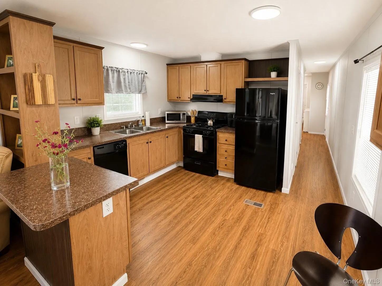 Kitchen featuring wood-finish flooring, light wood cabinetry with dark hardware, a double basin sink, black appliances, and a built-in shelving unit Kitchen featuring wood-finish flooring, light wood cabinetry with dark hardware, a double basin sink, black appliances, and a built-in shelving unit