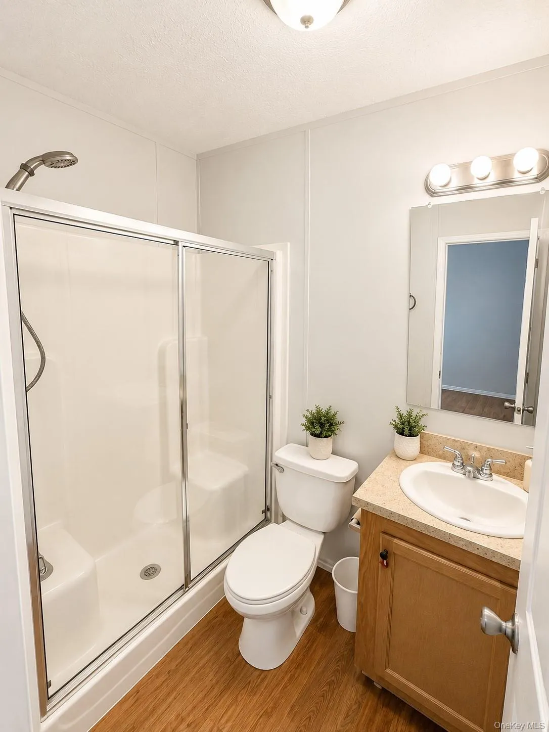 Full bathroom featuring a walk-in shower with sliding glass doors, a single vanity with a solid surface countertop, and wood-finish flooring Full bathroom featuring a walk-in shower with sliding glass doors, a single vanity with a solid surface countertop, and wood-finish flooring