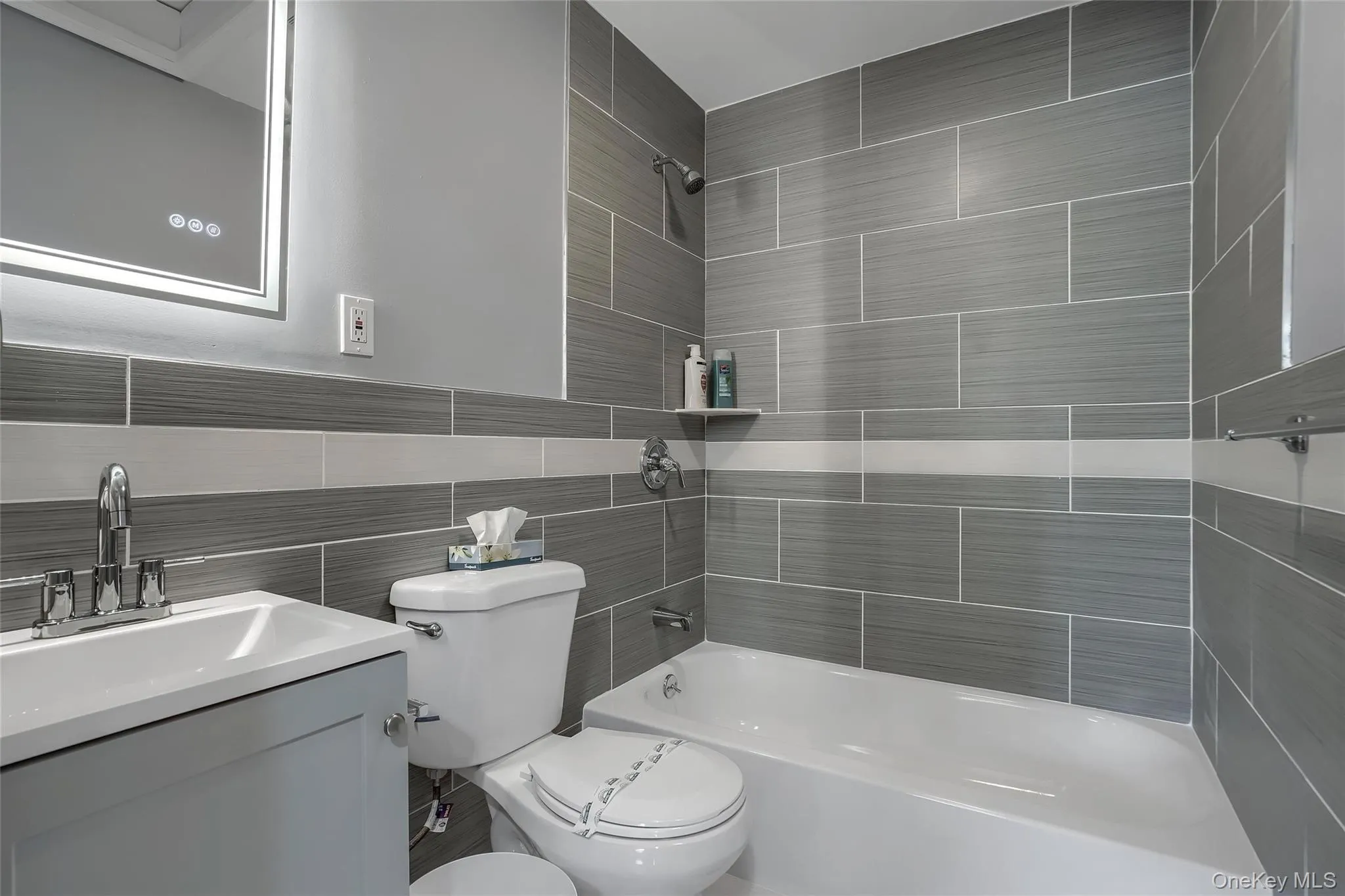 Full bathroom featuring a rectangular white sink, chrome fixtures, a light gray vanity, a white toilet, and a white bathtub Full bathroom featuring a rectangular white sink, chrome fixtures, a light gray vanity, a white toilet, and a white bathtub