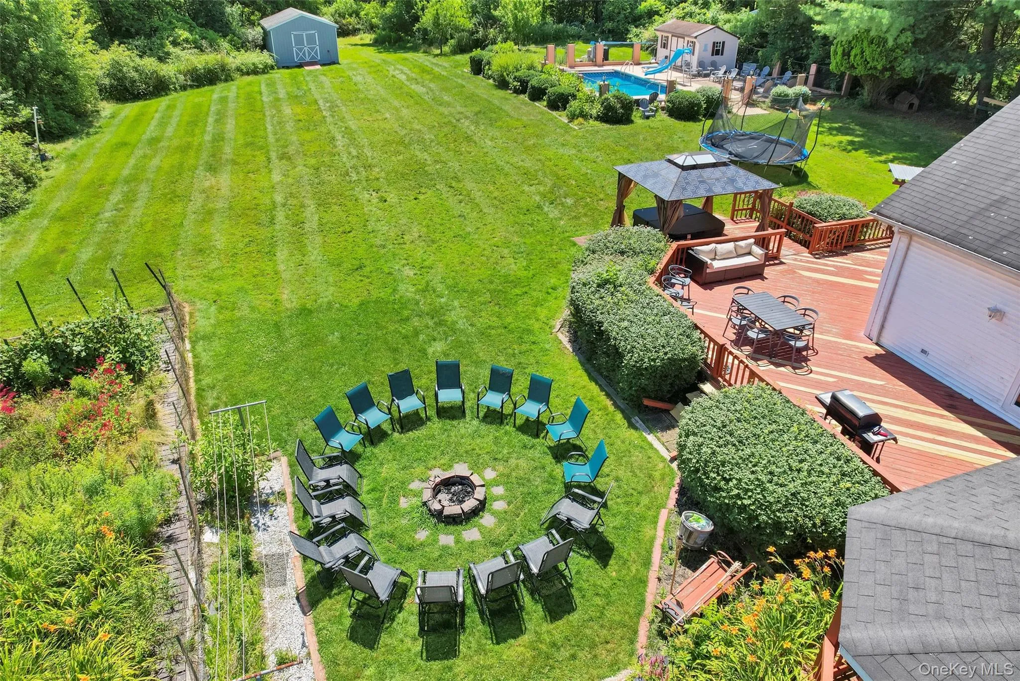 Expansive backyard featuring a large in-ground swimming pool with slide, a spacious multi-level wood deck, a sunken fire pit area, and a dedicated garden space Expansive backyard featuring a large in-ground swimming pool with slide, a spacious multi-level wood deck, a sunken fire pit area, and a dedicated garden space