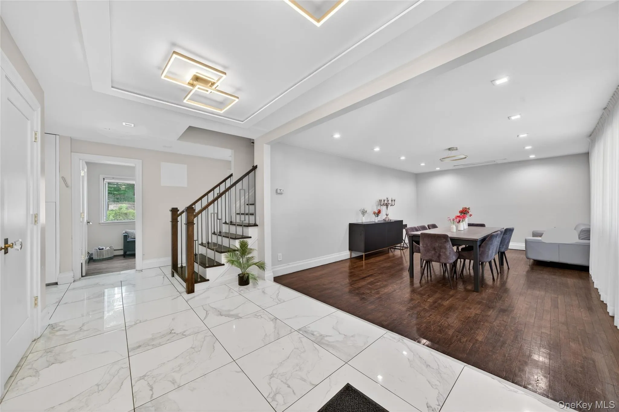 Spacious entryway with large-format marble-look tile flooring and a modern staircase featuring dark wood newel posts and metal balusters Spacious entryway with large-format marble-look tile flooring and a modern staircase featuring dark wood newel posts and metal balusters