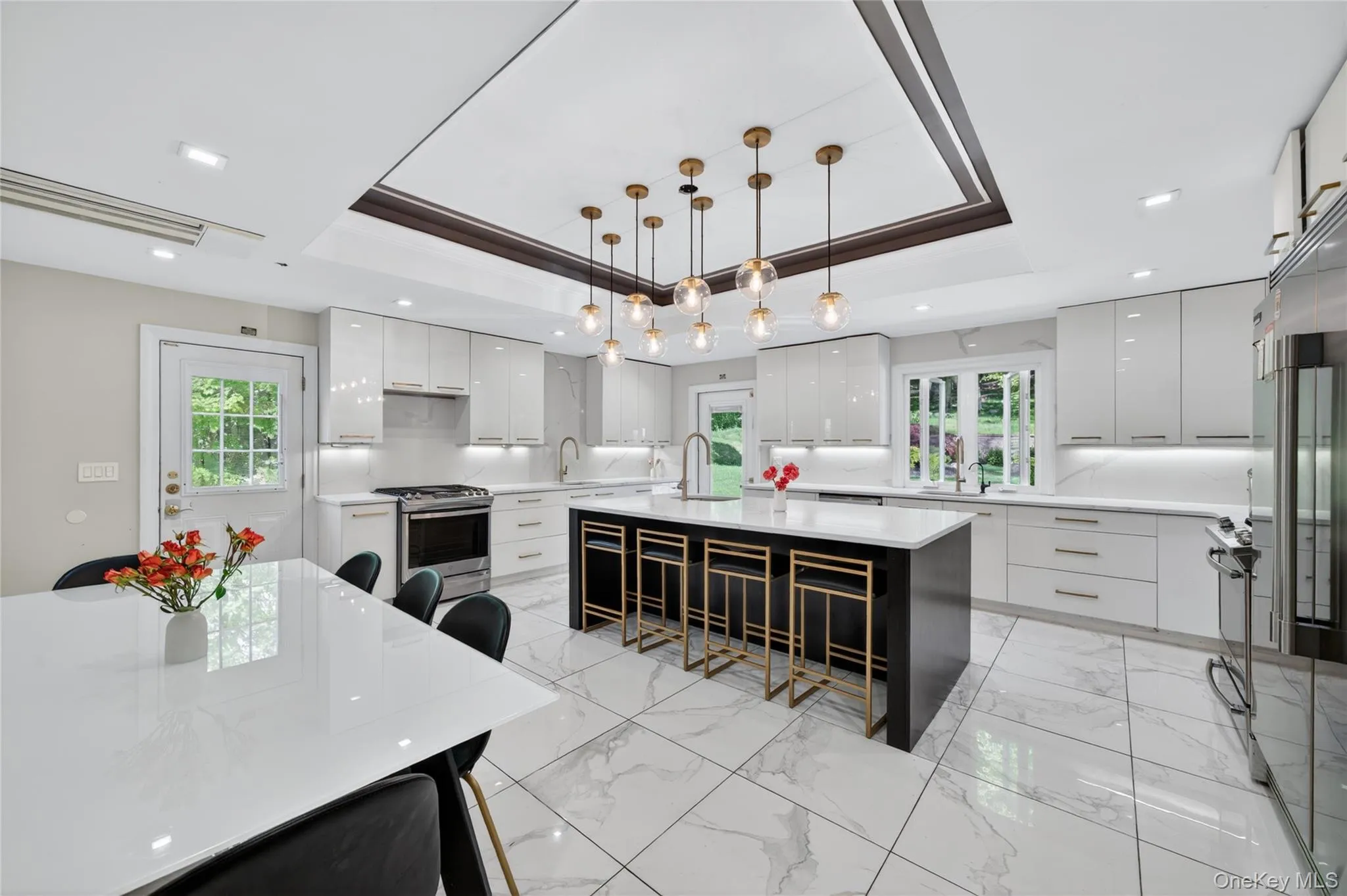 Modern kitchen featuring an expansive center island with seating, white high-gloss cabinetry, and a stainless steel appliance suite Modern kitchen featuring an expansive center island with seating, white high-gloss cabinetry, and a stainless steel appliance suite
