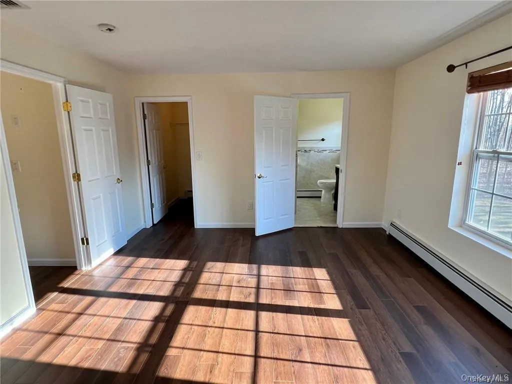 Primary bedroom with a baseboard heating, ensuite bath, and dark hardwood / wood-style floors Primary bedroom with a baseboard heating, ensuite bath, and dark hardwood / wood-style floors