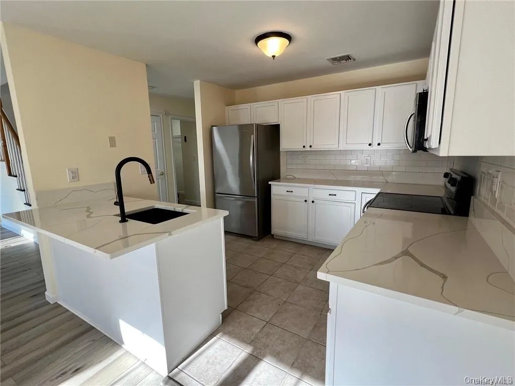 Kitchen with white cabinetry, light stone countertops, appliances with stainless steel appliances, sink, and tasteful backsplash Kitchen with white cabinetry, light stone countertops, appliances with stainless steel appliances, sink, and tasteful backsplash