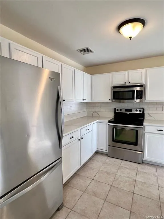 Kitchen with stainless steel appliances, light tile flooring, tasteful backsplash, and white cabinetry Kitchen with stainless steel appliances, light tile flooring, tasteful backsplash, and white cabinetry