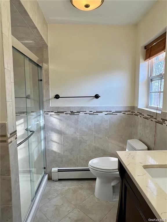 Primary Bathroom with tile walls, tile floors, a baseboard radiator, toilet, and vanity Primary Bathroom with tile walls, tile floors, a baseboard radiator, toilet, and vanity