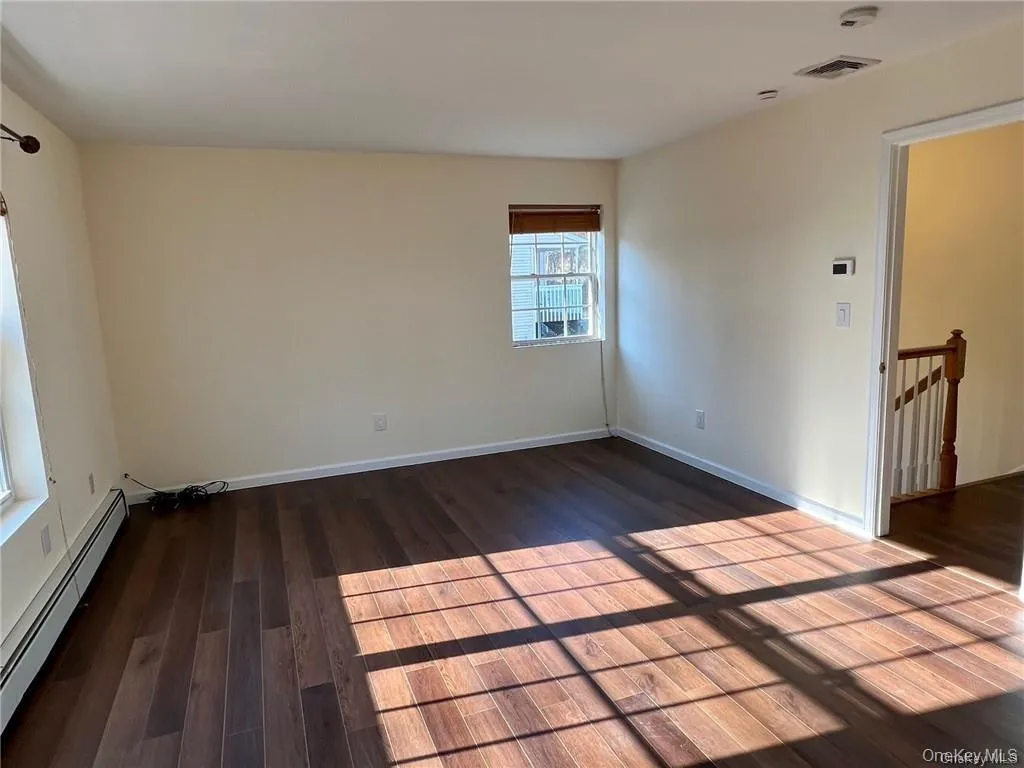 Primary bedroom with dark hardwood / wood-style floors and baseboard heating Primary bedroom with dark hardwood / wood-style floors and baseboard heating