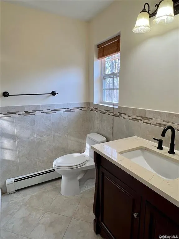 Primary Bathroom with tile walls, toilet, a baseboard heating unit, tile floors, and vanity Primary Bathroom with tile walls, toilet, a baseboard heating unit, tile floors, and vanity