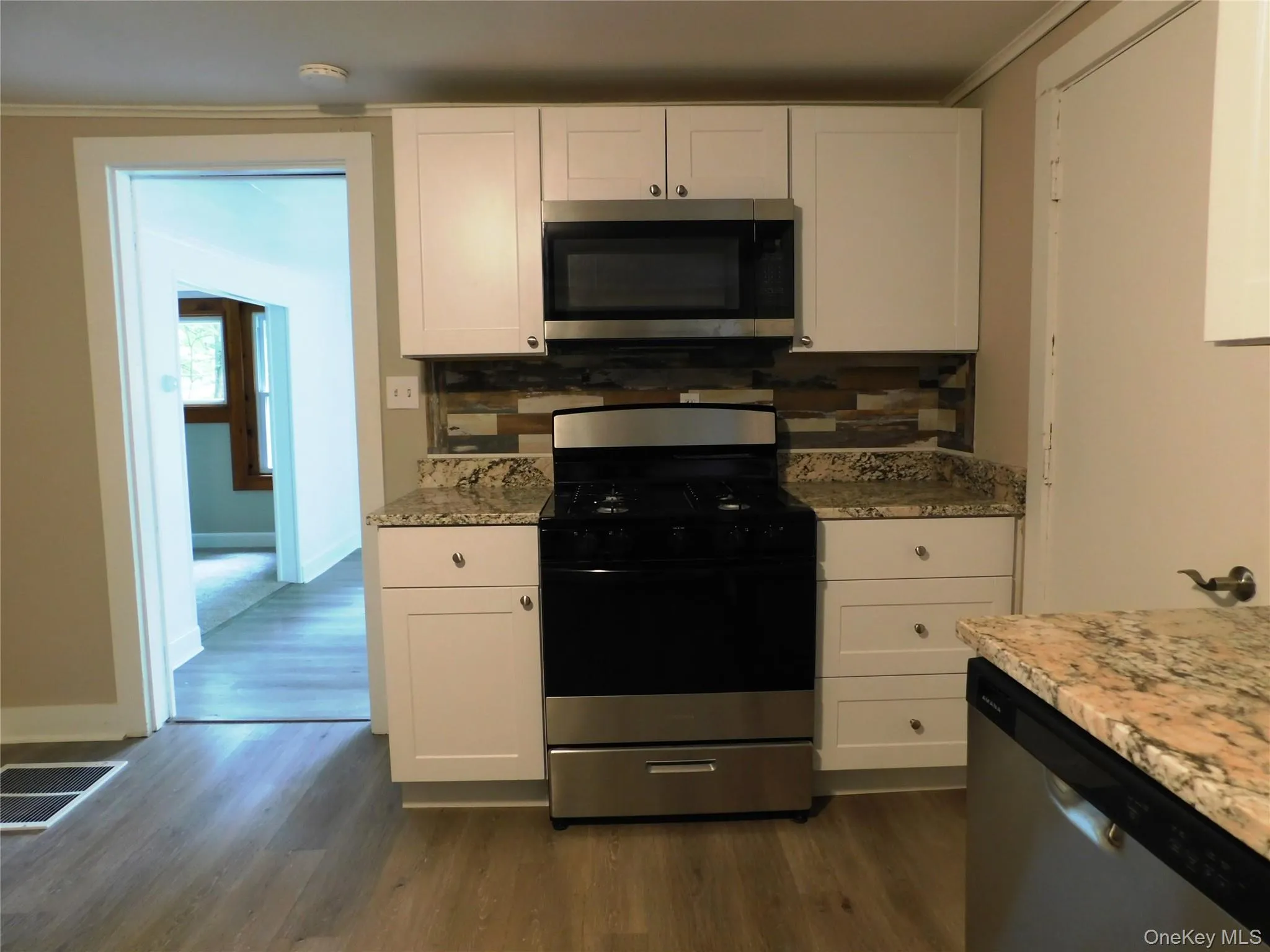 Kitchen featuring white cabinetry, granite countertops, a stainless steel gas range, an over-the-range microwave, and wood-finish flooring Kitchen featuring white cabinetry, granite countertops, a stainless steel gas range, an over-the-range microwave, and wood-finish flooring