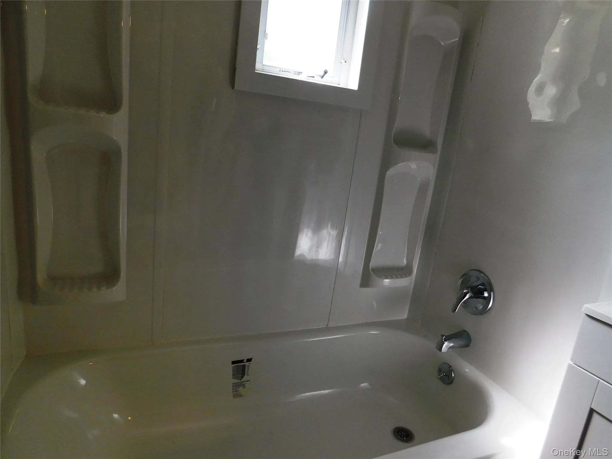 White bathtub with chrome fixtures, integrated wall shelving, and a window for natural light White bathtub with chrome fixtures, integrated wall shelving, and a window for natural light